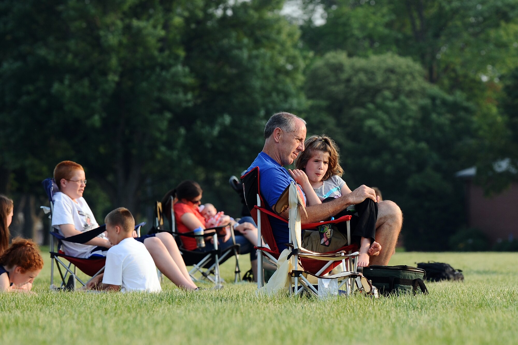 Dwight Cole, a civil servant with U. S. Strategic Command, sits with his seven-year-old daughter Cami while attending the Sundays on Parade concert performed by the Raptor ensemble of the United States Air Force Heartland of America Band on June 30, Offutt Air Force Base, Neb. More than a hundred concert goers lounged on blankets and lawn chairs while listening to Raptor play hit. (U.S. Air Force photo by Josh Plueger/Released)