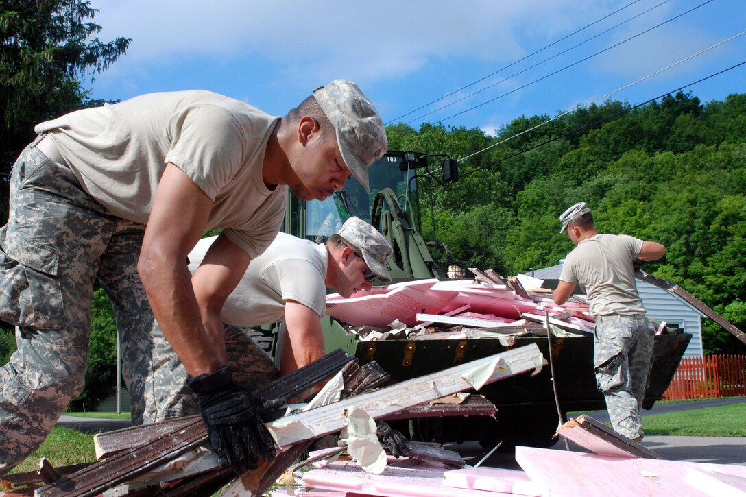 Army Pfc. Trey Hubbard, left, Spcs. Jason Briggs, center, and Brandon Demeree stack flood debris into the bucket of a front-end loader operated by Sgt. John Johnson near Mohawk, N.Y., July 5, 2013. Johnson is assigned to the New York National Guard's 152nd Engineer Company and Hubbard, Briggs and Demeree are assigned to the 206th Military Police Company.
