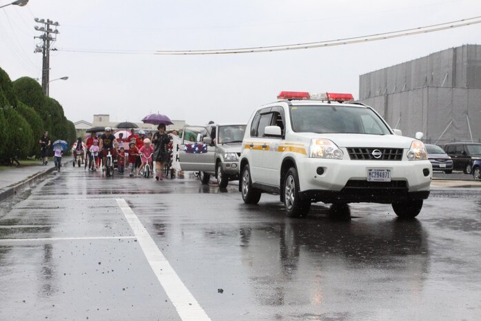 Participants ride bikes, scooters and walk during the Headquarters and Headquarters Squadron Independence Day Parade that circled the Parade deck block aboard station, July 4, 2013. Bikes, scooters and helmets were decorated in red, white and blue as they kept on trucking through the rain to show their American pride.