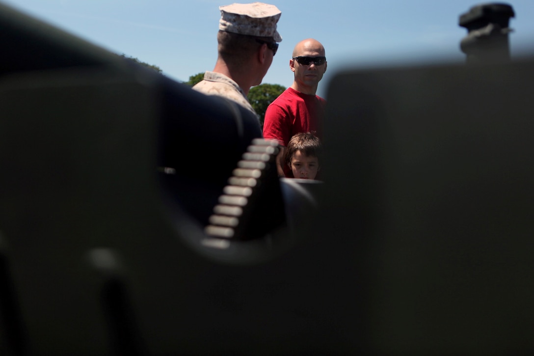 Capt. Miguel A. Cruz, Headquarters and Support Battalion Alpha Company commanding officer, and his son, Carlos, listen to a Golf Battery 2nd Battalion 10th Marines Regiment cannoneer Marine talk about the 155 mm Howitzer used during a Memorial Day 21 gun salute at the parade deck May 27. More than two dozen residents and veterans attended the ceremony. Teams of three cannoneer Marines fired blank rounds from four Howitzers. Blank rounds are used during ceremonies for their visual effect and for safety. The garrison flag flew at half-mast during the ceremony.