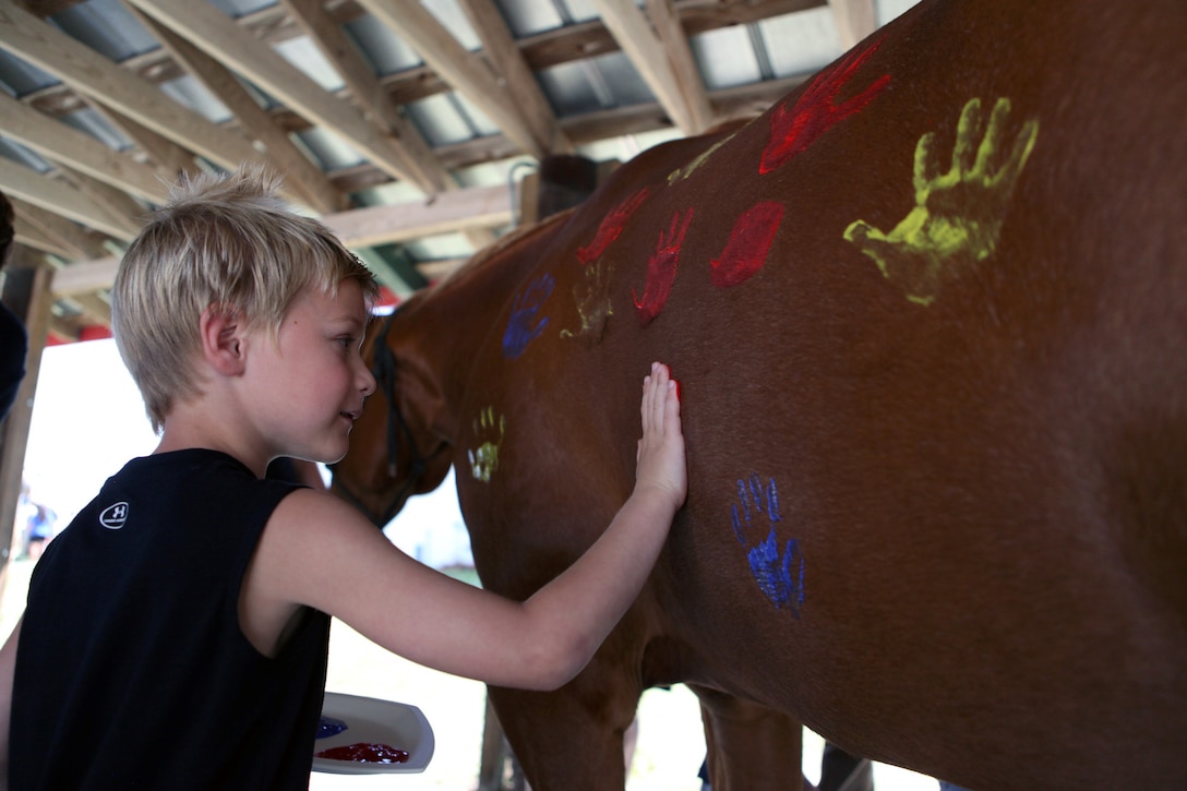 An Exceptional Family Member Program child presses his hand covered in paint onto the side of a Scarlet and Gold Riding Club horse for a sensory science class at the SGRC aboard Marine Corps Base Camp Lejeune, May 15. More than 30 EFMP children and parents attended the science class. Approximately 41 horses are housed at the SGRC