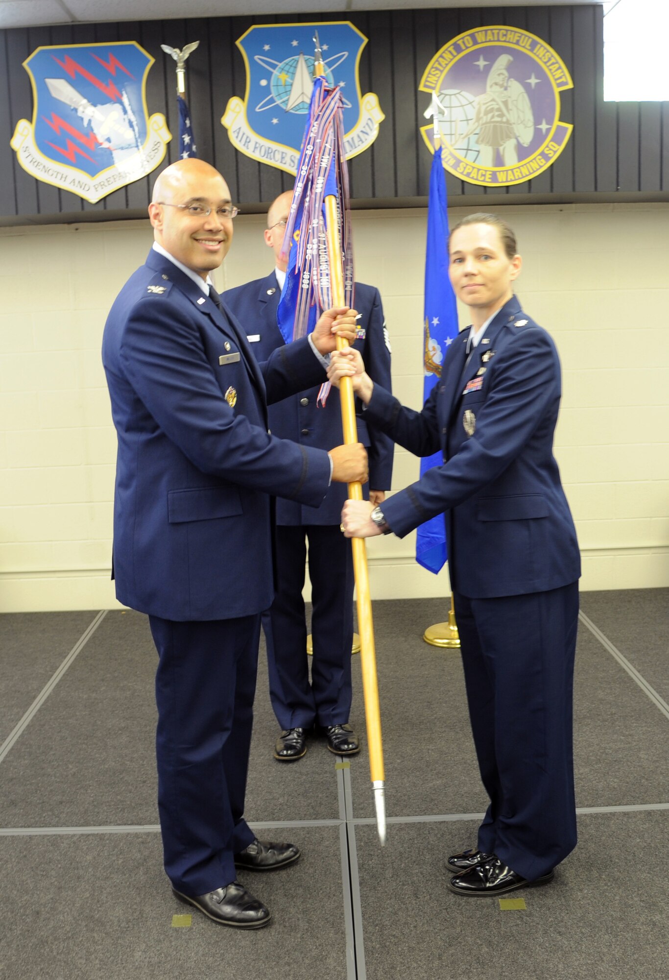 Col. David N. Miller Jr., commander of the 21st Space Operations Wing at Peterson Air Force Base, Colo., passes the 10th Space Warning Squadron guidon to Lt. Col. Michelle Kneupper during a change-of-command ceremony July 10, 2013, at Cavalier Air Force Station, N.D. Kneupper assumed command of the squadron from Lt. Col. Lorinda Frederick. (U.S. Air Force photo/Tim Flack)