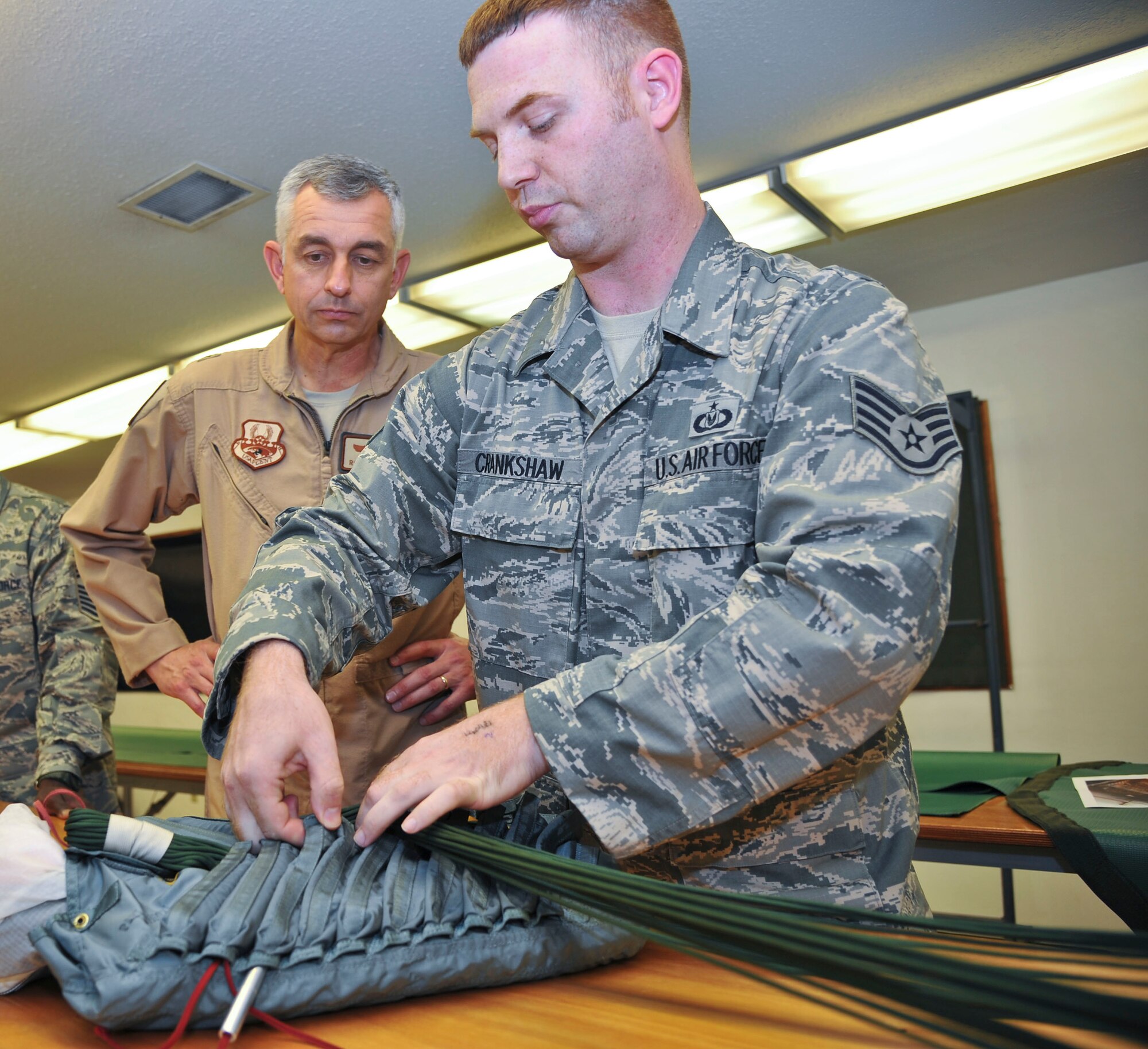 Staff Sgt. Henry Crankshaw demonstrates proper BA-22 parachute line stowing technique to Brig. Gen. Roger Watkins during the general’s visit to the 379th Expeditionary Operations Support Squadron’s Aircrew Flight Equipment at the 379th Air Expeditionary Wing in Southwest Asia, July 5, 2013. The 379th OSS AFE is the sole parachute back shop in the U.S. Central Command’s area of responsibility, supporting 11 other bases and is the primary inspector for equipment down range. Watkins is the 379th AEW commander and Crankshaw is the 379th EOSS AFE NCO in charge deployed from Elmendorf Air Force Base, Alaska. (U.S. Air Force photo/Tech. Sgt. Joselito Aribuabo)