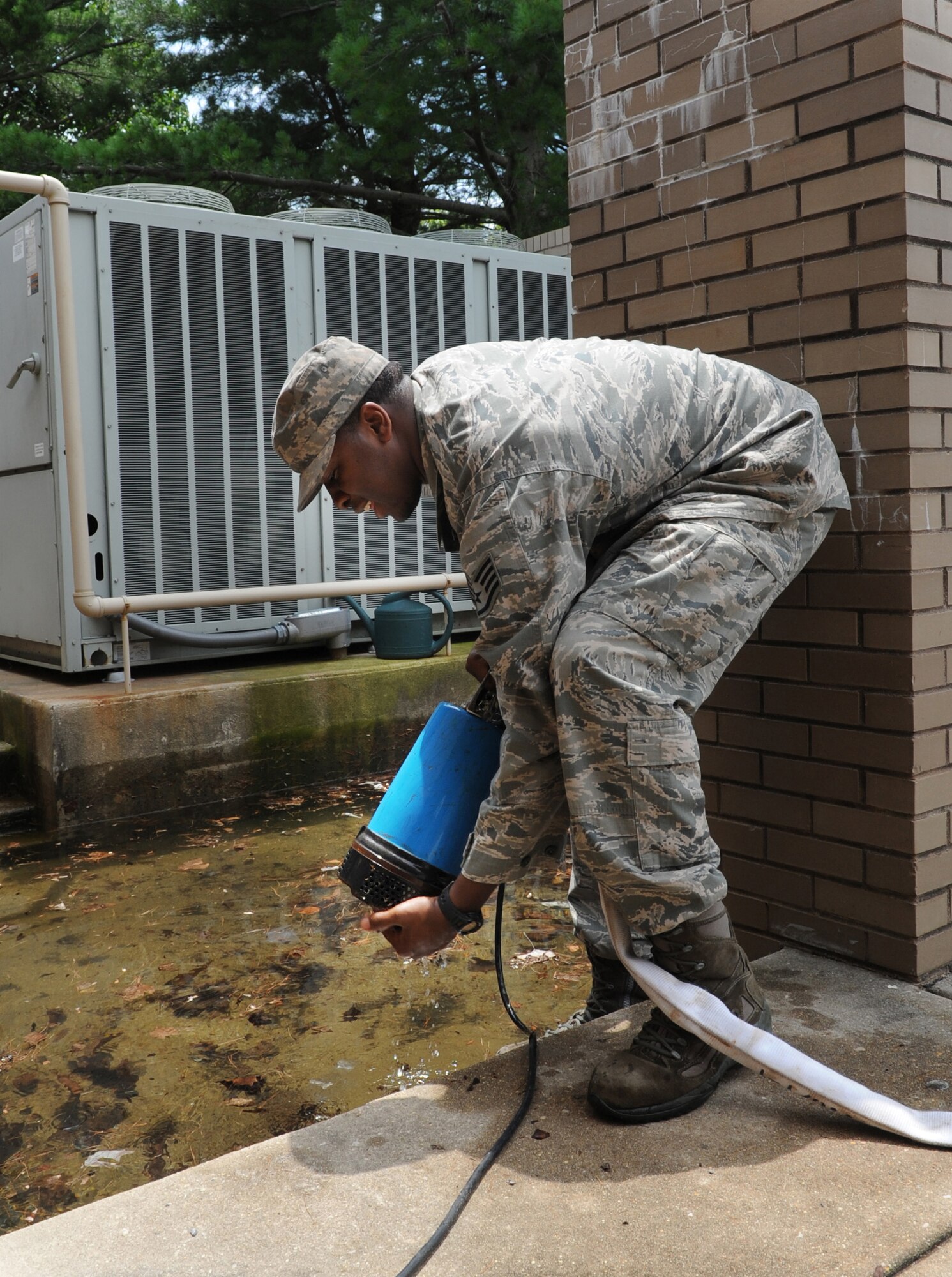 Staff Sgt. Alan Roberts; 87th Civil Engineer Squadron heating, ventilation and air condition Journeyman lowers a sump pump into a flooded area at the back of building 3011 on July 8, 2013 at  Joint Base McGuire-Dix-Lakehurst. The flood was caused by a broken valve on a domesticated water pump.  (U.S. Air Force photo by Kim Wright /Released)
