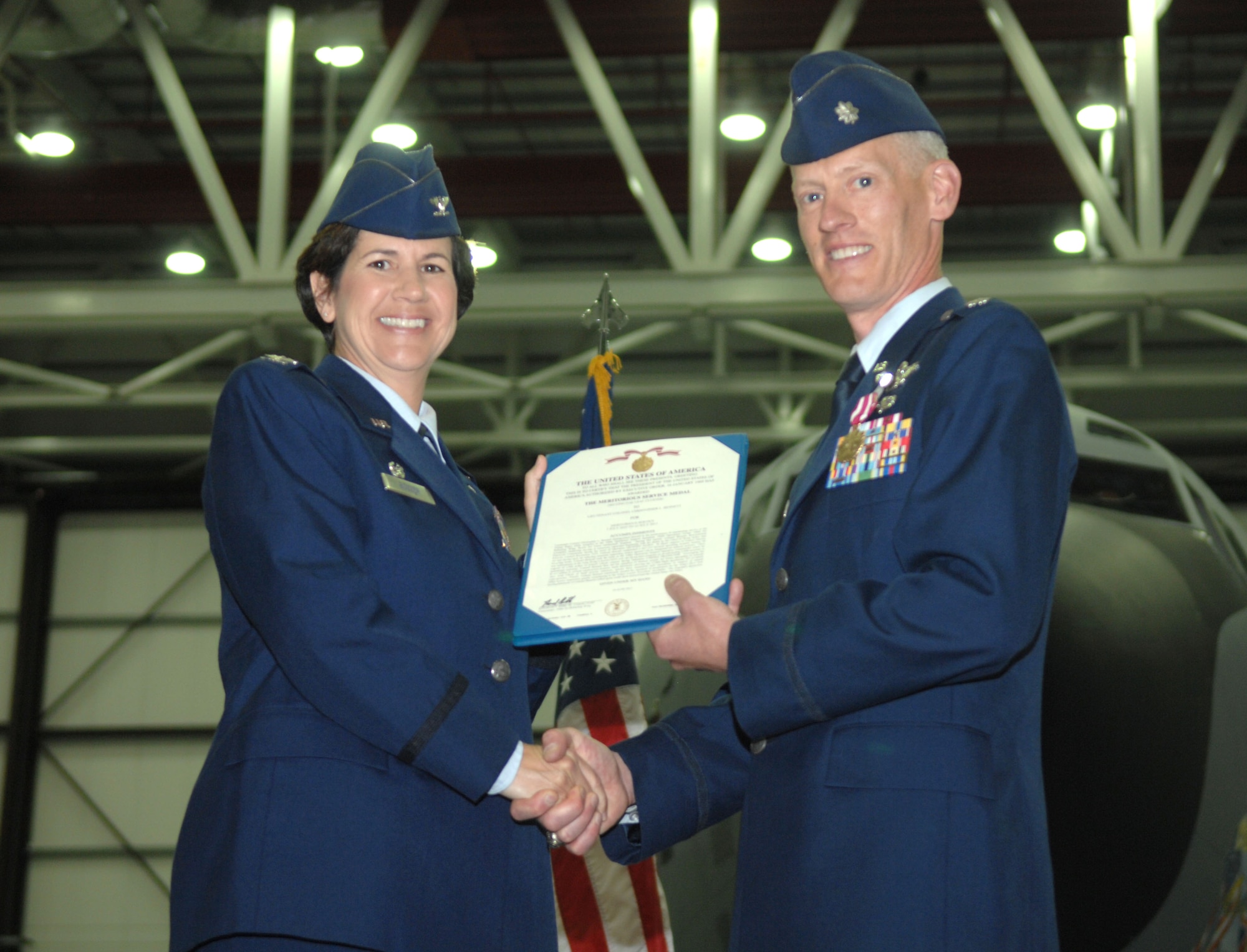 From left, Col. Nancy Bozzer, 100th Operations Group commander, presents the Meritorious Service Medal to Lt. Col. Christopher Bennett, 100th Operations Support Squadron commander, during the 100th OSS change of command July 12, 2013, in Hanger 814 on RAF Mildenhall, England. Bennett was the 100th OSS commander from 2011 to 2013. (U.S. Air Force photo by Airman 1st Class Dillon Johnston/Released)