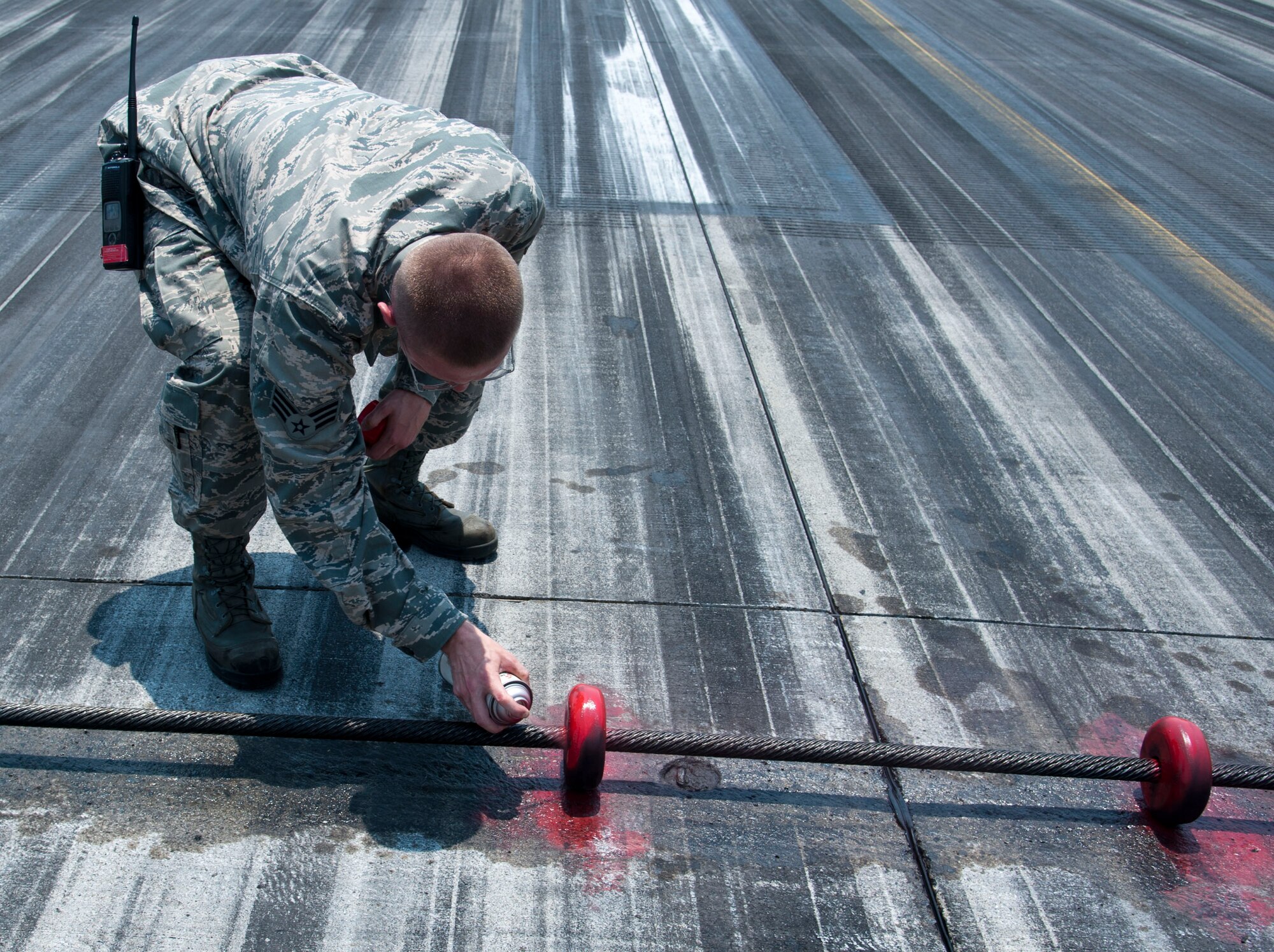 YOKOTA AIR BASE, Japan – Senior Airman Johnathan Riley, an electrical power production technician with 374 Civil Engineer Squadron, spray paints the two center doughnuts at Yokota Air Base, Japan, July 10, 2013.  The two center doughnuts are marked to help pilots identify the midpoint of the cable part of the arresting gear mechanism that assists with rapidly decelerating aircraft during landing.  (U.S. Air Force photo by Airman 1st Class Soo C. Kim)