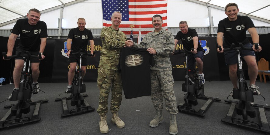 Royal Air Force Group Capt. Paul Atkinson, middle, Air Surveillance and Control System Force Commander shakes hands with Lt. Col. Berry McCormick, 727th Expeditionary Air Control Squadron commander at an undisclosed location in Southwest Asia June 27, 2013. The team of four Royal air force members, in the background, set out to exercise their way back to Lincoln, England, roughly 3,400 miles away, in honor of RAF and U.S. Air Force members who have been injured or killed in contingency operations overseas. They inspired the 727th EACS to start their own effort to honor a member back in the U.S. (U.S. Air Force photo/Senior Airman Jacob Morgan) 
