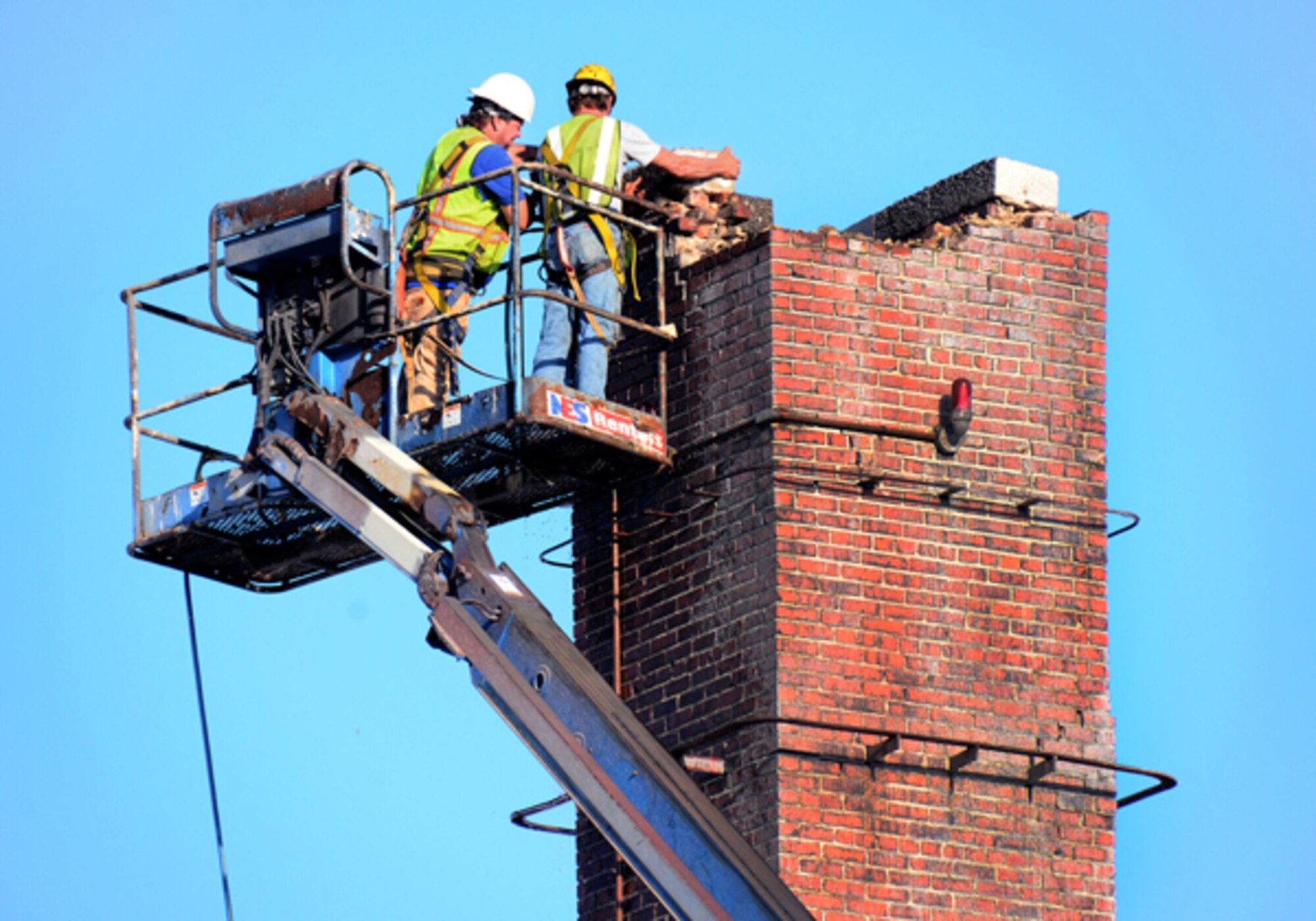 Contractors from A1 Construction trim chimneys at the 94th Airlift Wing headquarters building and cap them with metal ventilators. The ventilators will protect birds and debris from falling into chimneys. (U.S. Air Force photo/Brad Fallin)