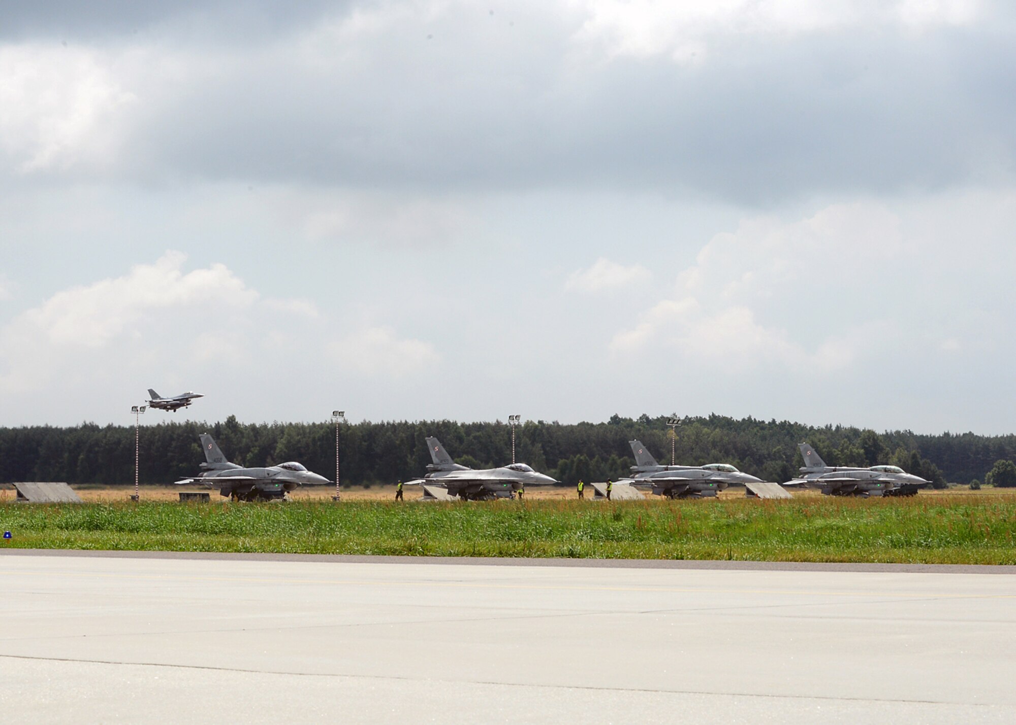 LASK AIR BASE, Poland -- A U.S. Air Force F-16 Fighting Falcon fighter aircraft from Aviano Air Base, Italy, begins landing procedures here July 12, 2013. The Polish air force F-16s rest on the taxiway before beginning a training flight. The United States and Poland are strengthening their combined air power by exercising together during a two-week aviation detachment rotation. (U.S. Air Force photo by Staff Sgt. Daryl Knee/Released)