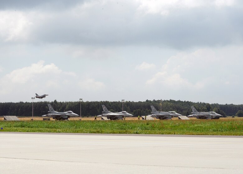 LASK AIR BASE, Poland -- A U.S. Air Force F-16 Fighting Falcon fighter aircraft from Aviano Air Base, Italy, begins landing procedures here July 12, 2013. The Polish air force F-16s rest on the taxiway before beginning a training flight. The United States and Poland are strengthening their combined air power by exercising together during a two-week aviation detachment rotation. (U.S. Air Force photo by Staff Sgt. Daryl Knee/Released)