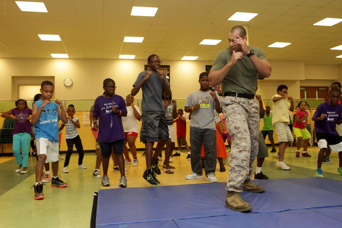 Sgt. Roberto Rodriguez, adjutant for Headquarters and Service Battalion, 4th Marine Division, Marine Forces Reserve, demonstrates a series of exercises to students from St. Peter Claver Church school, July 11. Marines visited the students to perform techniques from the Marine Corps Martial Arts Program to build rapport with the local community. (U.S. Marine Corps photo by Cpl. John McCall)