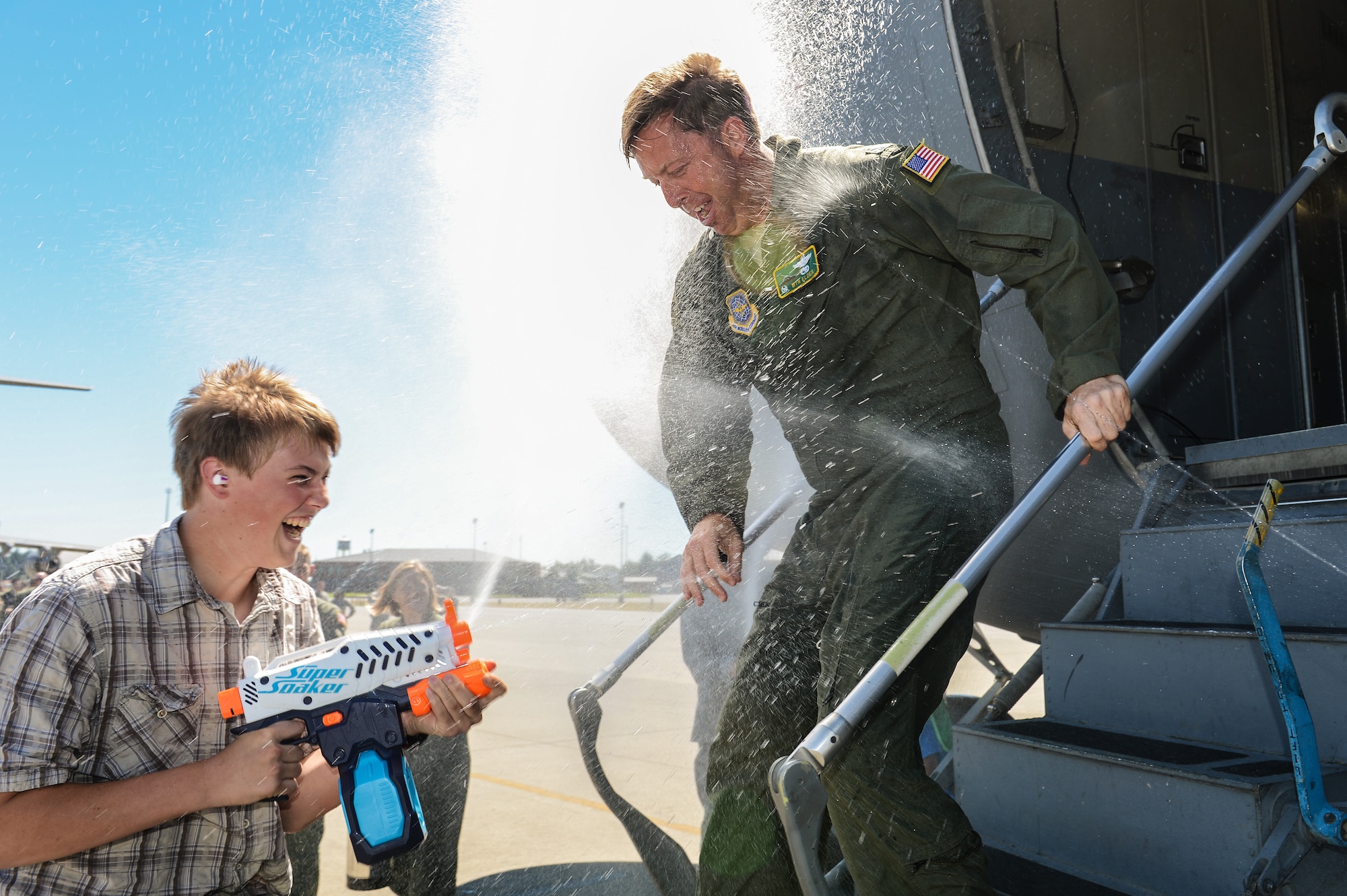 Col. Wyn Elder, 62nd Airlift Wing commander, is sprayed with a water gun by his son Travis upon return from his final flight as the wing commander, July 15, 2013, at Joint Base Lewis-McChord, Wash. As is the tradition after a "fini flight," Elder was met by family members and Airmen who immediately "ambushed" him with a barrage of water guns and hoses upon exiting the aircraft. (U.S. Air Force photo/TSgt Sean Tobin)