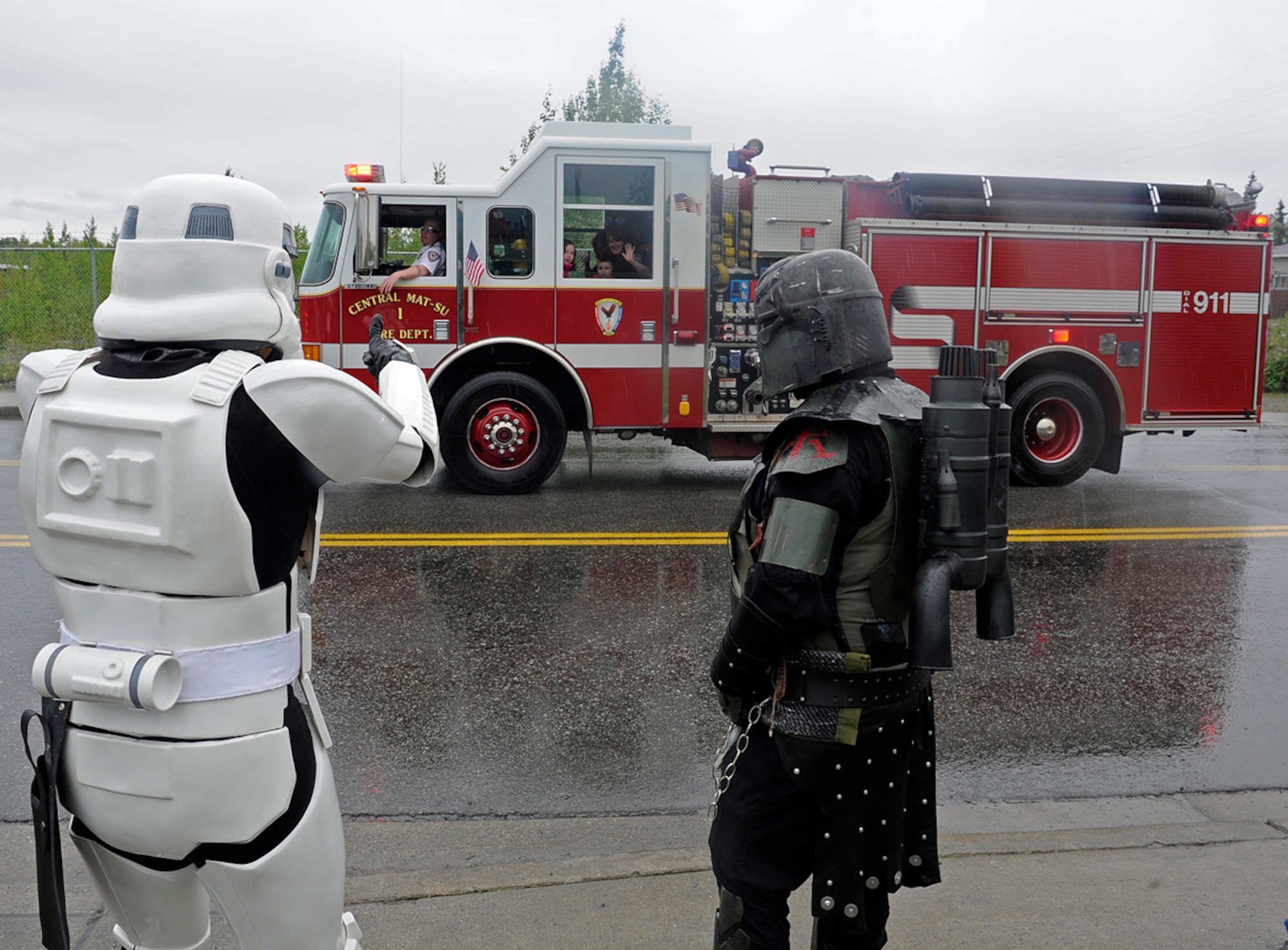 Air Force Staff Sgt. Patrick Walsh, 673d Communications Squadron cyber transport supervisor, waves to a Central Mat-Su Fire Department firetruck with Jade Pardue, a local 501st Legion, Vader's fist, member in Wasilla, Alaska, July 4, 2013. The 501st is an all volunteer organization that makes movie accurate costumes and wears them to promote interest in Star Wars, encourage use of the costumes made, and to contribute to the local community. (U.S. Air Force photo/Staff Sgt. Zachary Wolf)