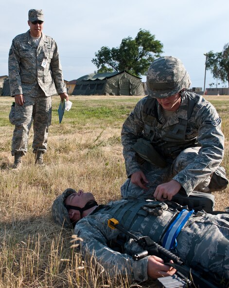 Tech. Sgt. Brian Thomas, 28th Civil Engineer Squadron Exercise Evaluation Team member, observes Airman 1st Class Thomas Goss, 28th CES structural technician, perform self-aid and buddy care to Airman 1st Class Joshua Weum, 28th CES heating, ventilation and air conditioning technician, during the Phase II portion of an operational readiness exercise at Ellsworth Air Force Base, S.D., July 11, 2013. The Phase II ORE placed Airmen in a simulated deployed environment that tested their ability to perform duties in a variety of stressful deployed scenarios. (U.S. Air Force photo by Airman 1st Class Alystria Maurer/Released)