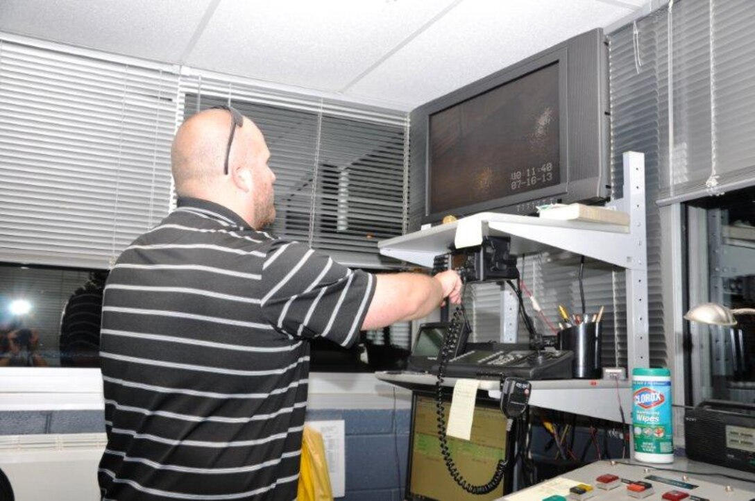 Dallas Barfield, U.S. Army Corps of Engineers Nashville District lock operator at Kentucky Lock, Grand Rivers, Ky., closely watches his monitor July 16, 2013 as motor vessel “Miss Katie” and its tow with the 50-foot electromagnetic particle ring Muong-2 are lowered to tailwater level en route to Chicago. The Muong-2 is a very powerful electromagnetic ring capable of carrying 5,200 amps of current and it creates a very strong magnetic field that allows storing a special particle called a muon. For additional information on the Muon g-2, and how the Nashville District contributed to its journey, go to
http://www.npr.org/2013/07/02/197719271/15-ton-particle-ring-travels-to-chicago-by-land-and-by-sea>. 