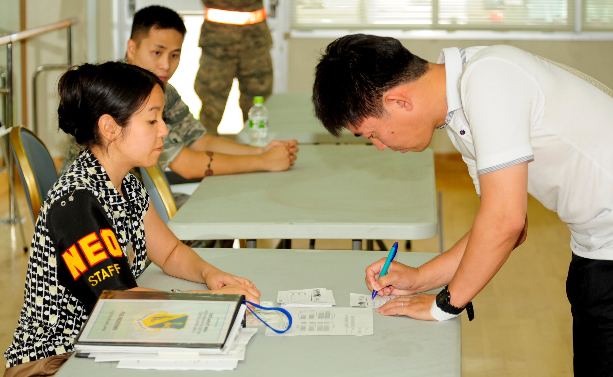 Joyce Kuwae, 374th Force Support Squadron, helps a Non-combative Evacuation Operation scenario role player fill out a bed down assignment card during the Operational Readiness Exercise at the Taiyo Community Center on Yokota Air Base, Japan, July 15, 2013. These cards are used to when assigning cots to individuals for accountability purposes. (U.S. Air Force photo by Senior Airman Michael Washburn/released) 