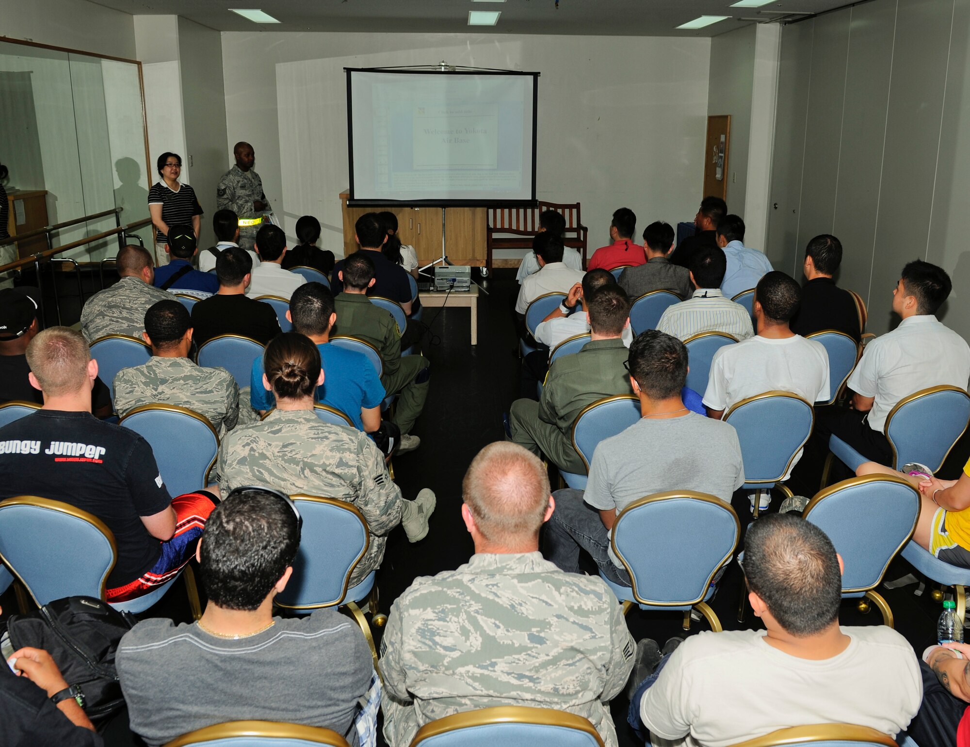 Tech. Sgt. Jonathan Cooley, 374th Force Support Squadron, presents Non-combative Evacuation Operation scenario role players with an informational slideshow during the Operational Readiness Exercise at the Taiyo Community Center on Yokota Air Base, Japan, July 15, 2013. Airmen along with Japan Air Self-Defense Force members participated in the NEO portion of the exercise. (U.S. Air Force photo by Senior Airman Michael Washburn/released)