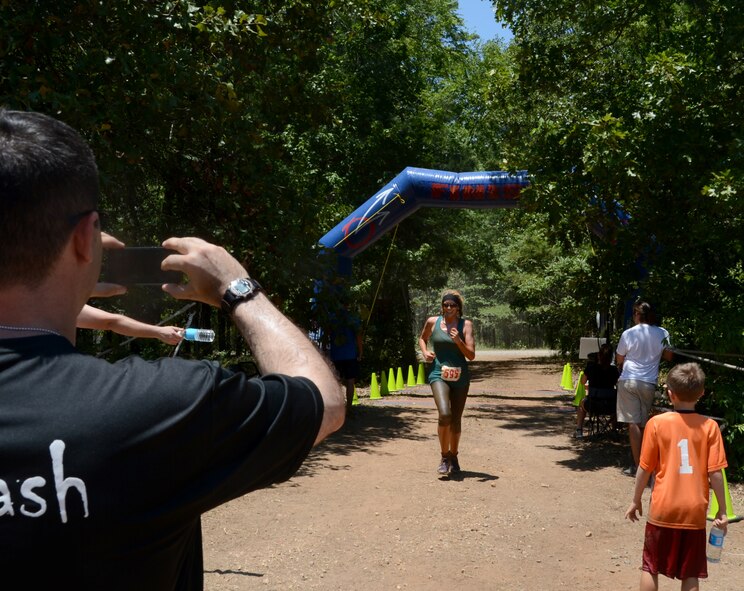 Col. Andrew Gebara, 2nd Bomb Wing commander, takes a photo of his wife, Dr. Nikki Gebara, as she crosses the finish line during the alphARace at the East Reservation on Barksdale Air Force Base, July 13, 2013. The commander competed the previous evening in the night race while his wife made the top three in her wave to move on to the championship race. (U.S. Air Force photo/Staff Sgt. Amber Corcoran)