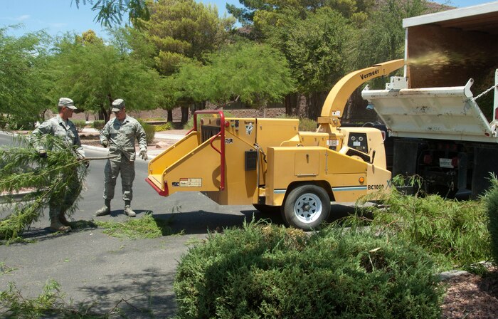 U.S. Air Force Airmen 1st Class Chet Wagnon and Cody Miller, 99th Civil Engineer Squadron pavements and equipment apprentices, load trimmed tree branches into a wood chipper in front of Bldg. 11, headquarters for the 99th Mission Support Squadron and the 99th Comptroller Squadron,  July 15, 2013, at Nellis Air Force Base, Nev. The CES pavements and equipment Airmen are responsible for the maintenance and construction of the base’s fences, paved roads and airfields along with the use and maintenance of heavy equipment. (U.S. Air Force photo by Airman 1st Class Timothy Young)