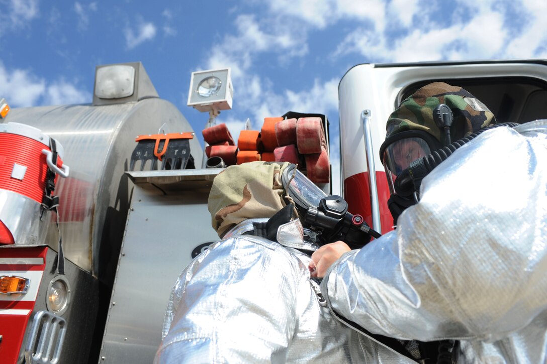 Airmen from the 28th Civil Engineer Squadron Fire Department help each other get into their mission oriented protection posture gear during the Phase II portion of an operational readiness exercise on Ellsworth Air Force Base, S.D., July 10, 2013. Fire protection Airmen are required to wear standard MOPP gear as well as fire resistant gear to help them stay safe and continue the mission during attacks. (U.S. Air Force photo by Airman 1st Class Rebecca Imwalle/Released)