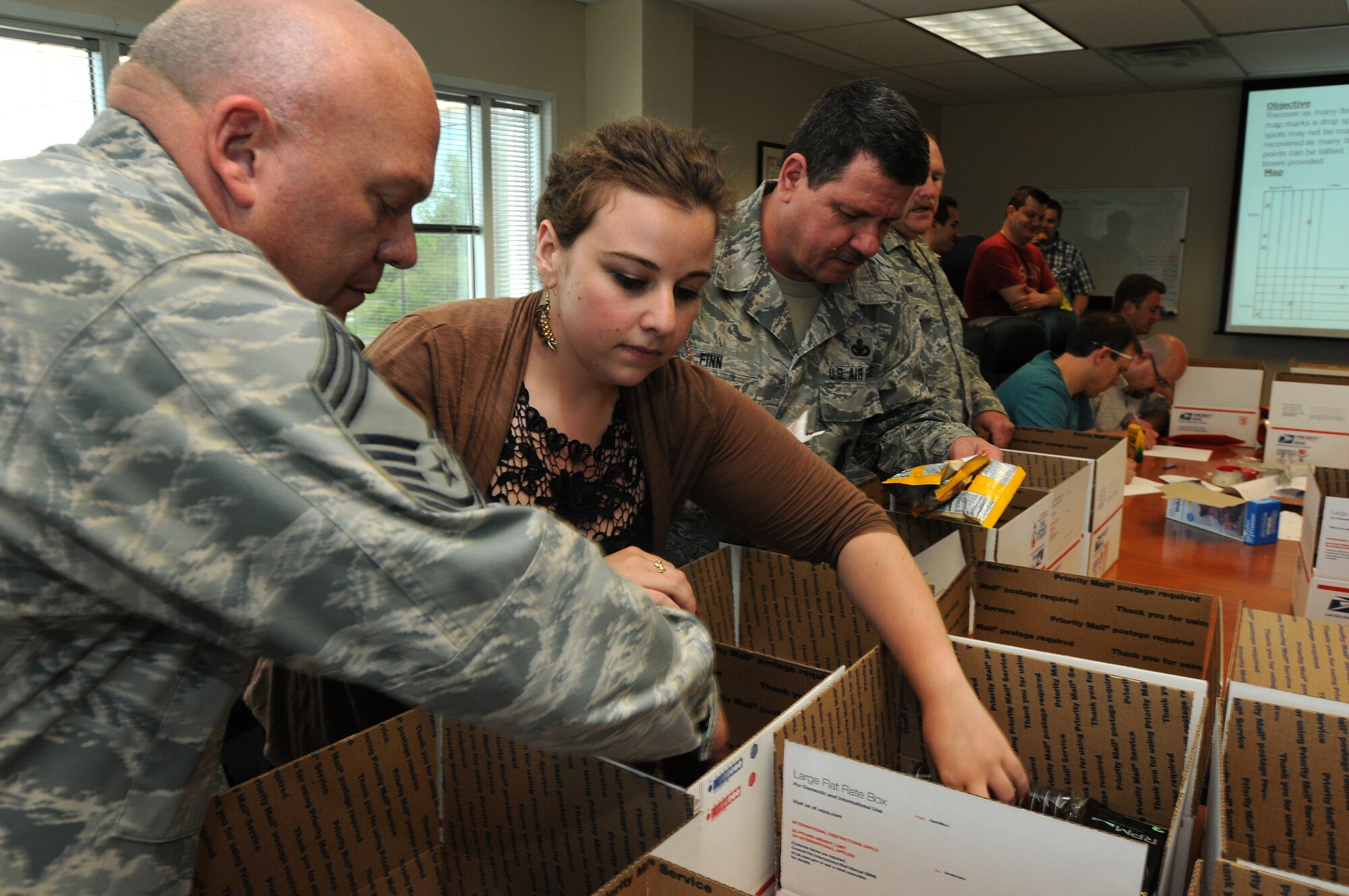 Wing volunteers spend their May 17 afternoon assisting employees from Verilgue, Inc. in building care packages destine for overseas-deployed military members. The 111th Fighter Wing Anti-Terrorism Officer, Chief Master Sgt. Paul G. Frisco, Jr. (left), Verilogue’s Global Field Coordinator,  Floriana Webb and Security Forces Superintendent, Chief Master Sgt. James Finn along with others stuffed 36 boxes with sweets, letters and trinkets to thank deployed servicemen and remind them of the strong support locally for their sacrifices.