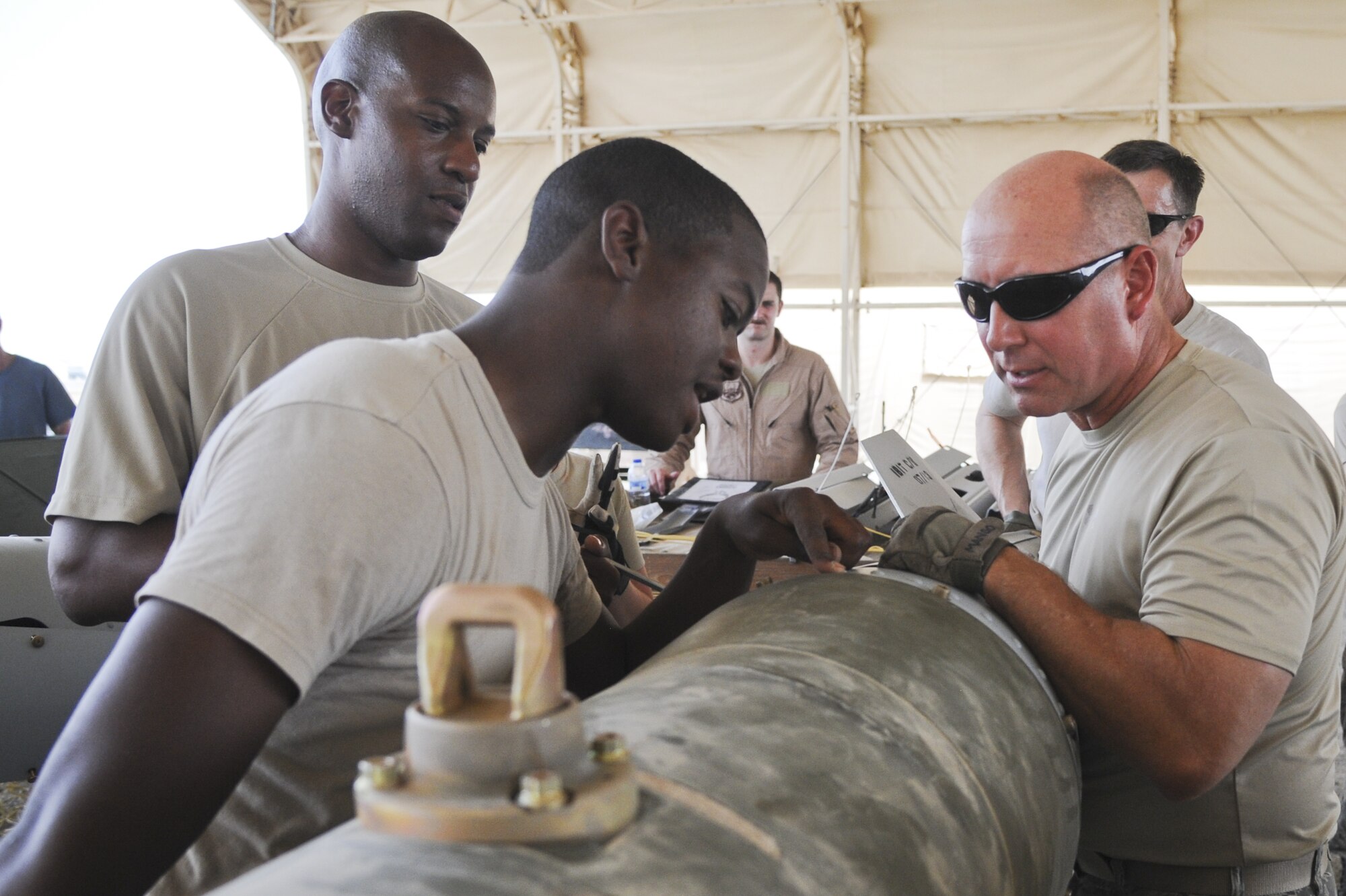 U.S. Air Force Staff Sgt. Arryn Meneese, front left, 380th Expeditionary Maintenance Squadron conventional maintenance crew chief, and U.S. Air Force Tech. Sgt. William Crawford, 380th Expeditionary Maintenance Squadron conventional maintenance assistant NCO in charge, show U.S. Air Force Chief Master Sgt. Garth Meade, 380th Air Expeditionary Wing command chief where to properly align a tail kit to a GBU-31 version 3 bomb at the temporary munitions storage area in an undisclosed location in Southwest Asia July 15, 2013. Pilots and other members of the 380th AEW took a tour of the temporary munitions storage area in the hopes of gaining more knowledge of what goes into building munitions. (U.S. Air Force photo by Senior Airman Jacob Morgan)