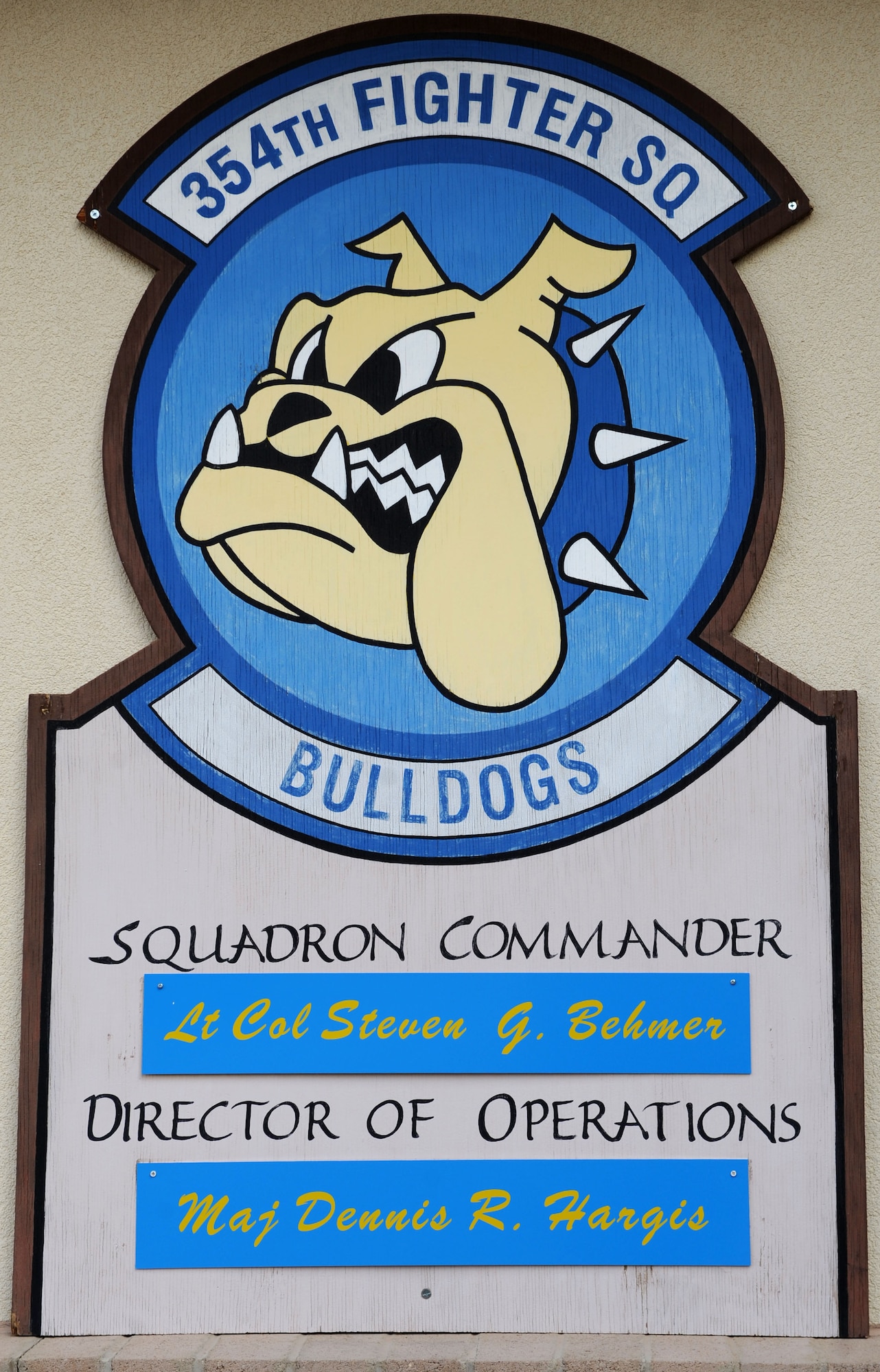 A placard showcasing the squadron patch and key leadership names hangs on the front of the 354th Fighter Squadron at Davis-Monthan Air Force Base, Ariz., July 17, 2013. The 354th FS, along with four other squadrons, is part of the 355th Operations Group. (U.S. Air Force photo by Airman 1st Class Saphfire Cook/Released)