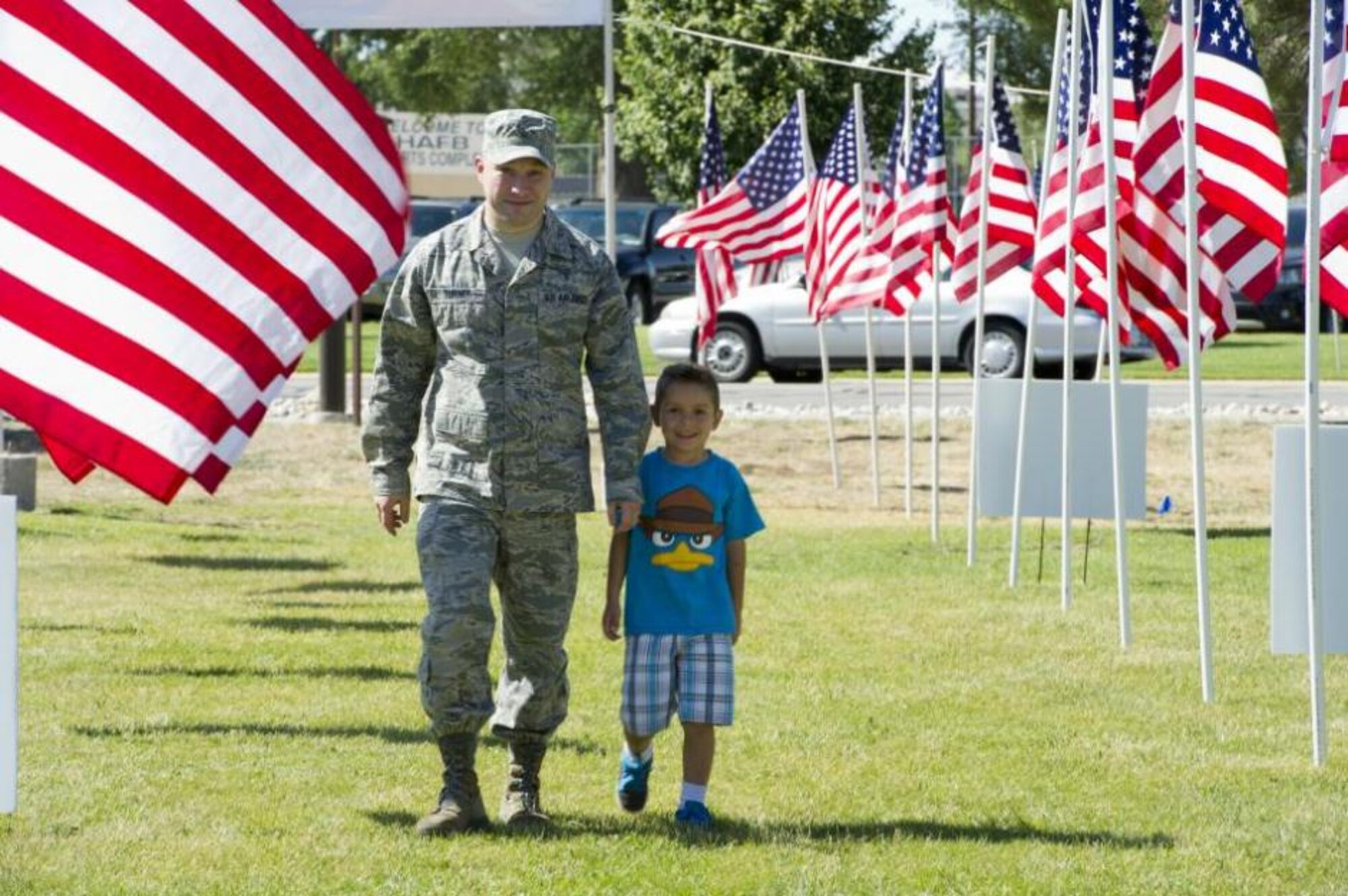 Staff Sgt. Daniel Turner and his son, Ethan Turner, walk through the flag-lined entrance to the Salute to Our Nation's Defenders Picnic July 12 at Centennial Park. More than 3,500 people attended the annual picnic, which included complimentary food, drinks and desserts, as well as activities for military members and their families. (U.S. Air Force photo by Tech. Sgt. Eric Burks/Released)