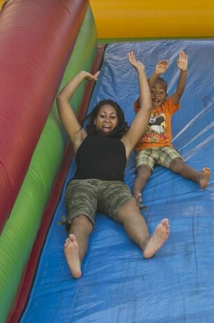 Karmesha Peterson (left) and her son Nathaniel Peterson Jr., go down an inflated slide during the 2013 Salute to the Nation’s Defenders Picnic July 12 at Centennial Park. Several different activities for families and their children were available including the slide, a climbing wall and a bouncy room. (U.S. Air Force photo by Tech. Sgt. Eric Burks/Released)