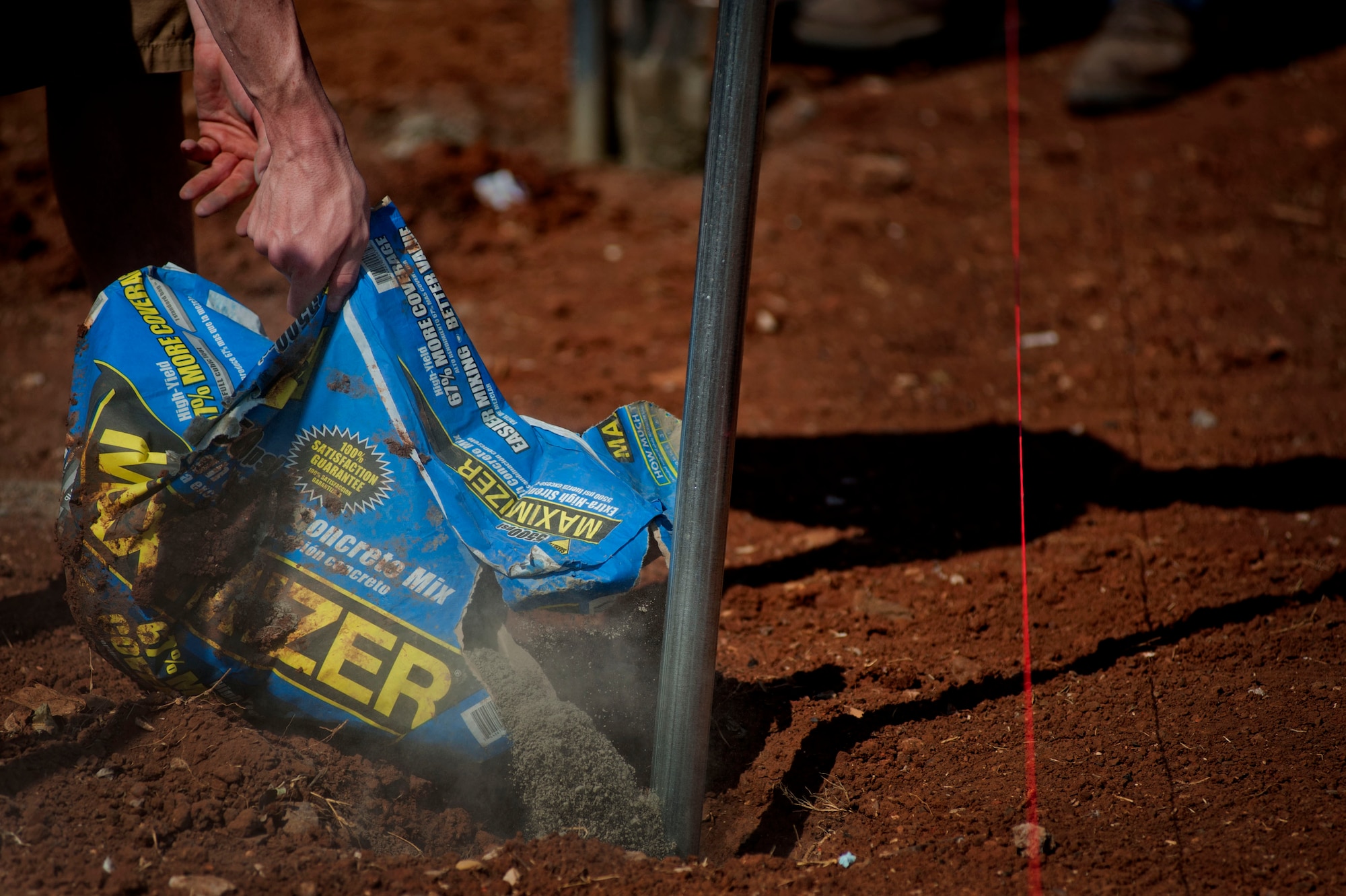 A participant in the construction effort pours concrete mix into the dirt July 13. Each individual outside had a specific role in building the houses. (U.S. Air Force photo by Airman 1st Class Jelani Gibson)  