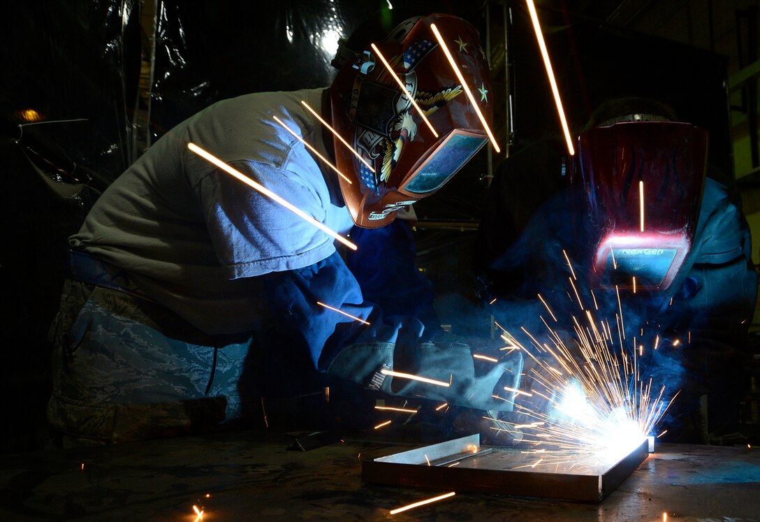Senior Airman Kyle Zastrow performs an elbow weld while Senior Airman Isa Holland observes his work July 12, 2013, in Southwest Asia. Zastrow is using a metal inert gas welder and being trained on welding, which is not typical work for his career field. Holland is his trainer and will provide guidance on several aspects of his job during their deployment. Both are members of the combat metals shop, which uses two different career fields for a broader capability. Zastrow and Holland are deployed to the 386th Expeditionary Maintenance Squadron. (U.S. Air Force photo/Master Sgt. Christopher A. Campbell)