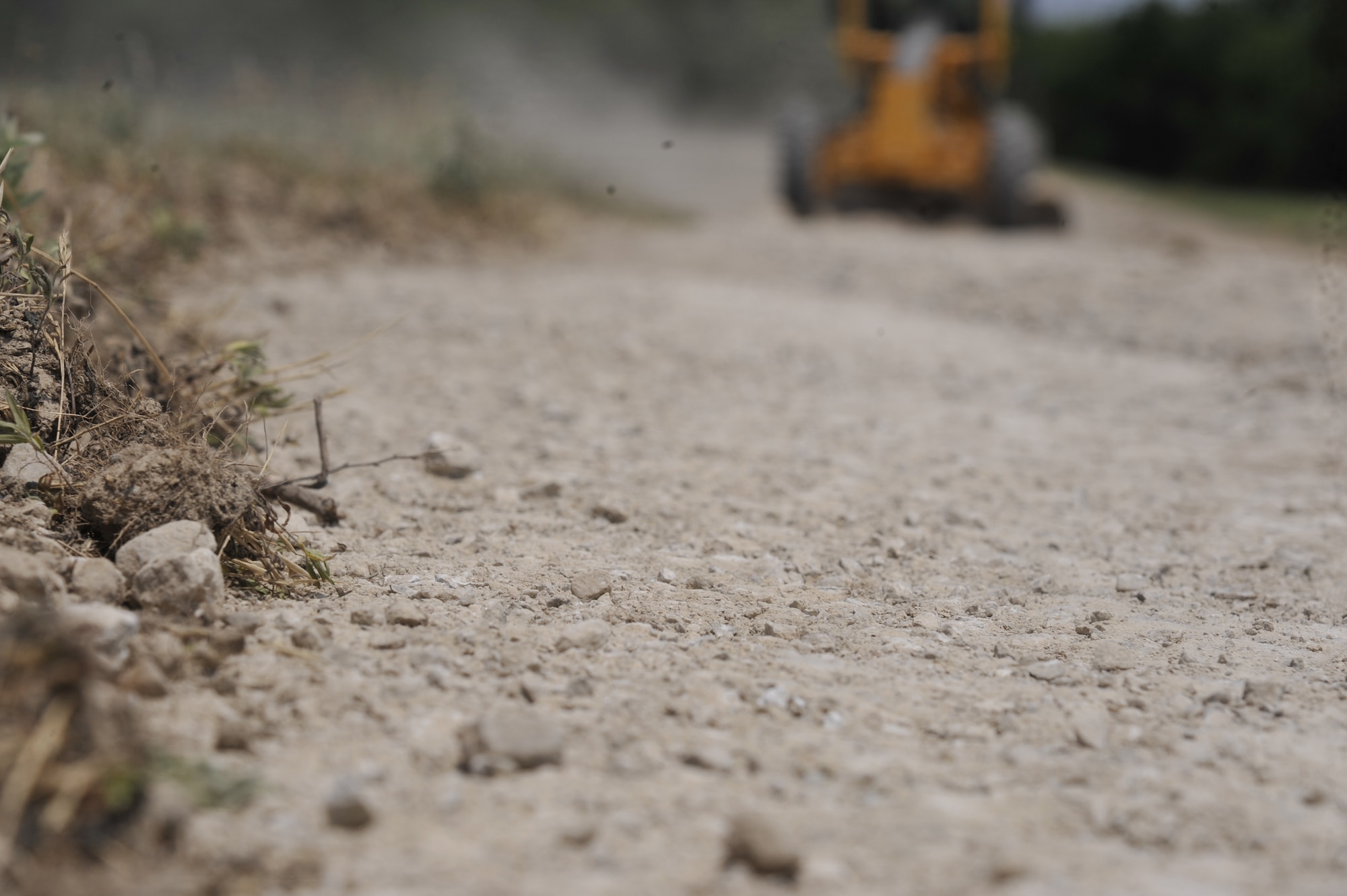 An airman levels rocks in the road using a grader at Whiteman Air Force Base, Mo., June 9, 2013. The grader is used to level the roads to drain rain puddles, making it easier to drive vehicles on. (U.S. Air Force photo by Airman 1st Class Keenan Berry/Released)