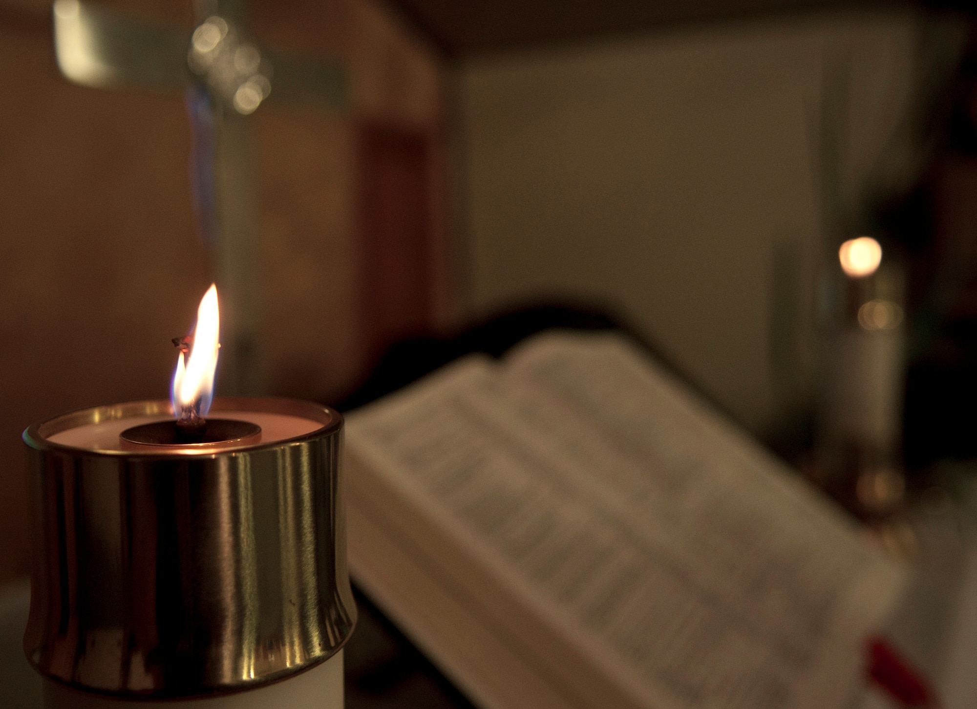 Twin candles stand on either side of a Holy Bible, positioned in front of a cross, during a chapel Protestant service at Transit Center at Manas, Kyrgyzstan, July 14, 2013. Christians believe that the burning candles represent the light of Jesus Christ, and the cross is a reminder of him. (U.S. Air Force photo/Staff Sgt. Robert Barnett)