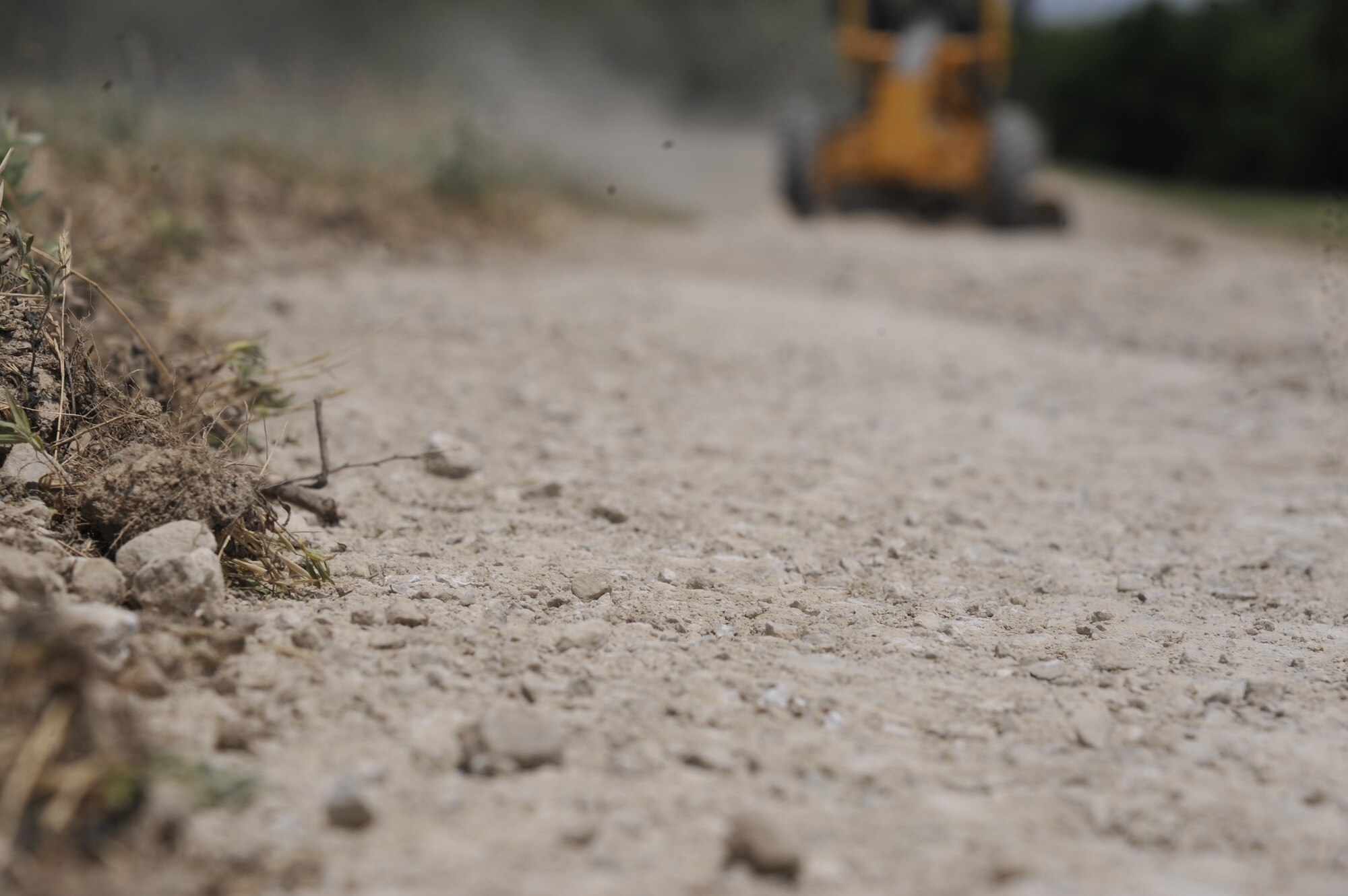 An airman levels rocks in the road using a grader at Whiteman Air Force Base, Mo., June 9, 2013. The grader is used to level the roads to drain rain puddles, making it easier to drive vehicles on. (U.S. Air Force photo by Airman 1st Class Keenan Berry/Released)