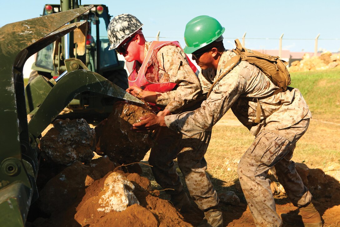 Lance Cpl. James S. Sipper, left, and Cpl. Sal J. Flores Jr. add rocks to the bucket of a multiterrain loader July 8 during the removal of a 60-meter-long wall near U.S. Army Garrison Torii Station’s main gate. Teamwork played an important part in the completion of the project, according to Sipper. Flores and Sipper are heavy-equipment operators with 9th Engineer Support Battalion, 3rd Marine Logistics Group, III Marine Expeditionary Force.