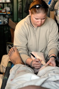 Illinois Army National Guard Spc. Whitney Meyers writes down vital information on the dressing applied to a 16-year-old truck driver of Herat city, during treatment for an injury he sustained to his foot. The Afghan National Police of the area brought Berza to the base where he was stabilized then medically evacuated to the Provincial Reconstruction Team in Farah where he was treated by U.S. surgeons.