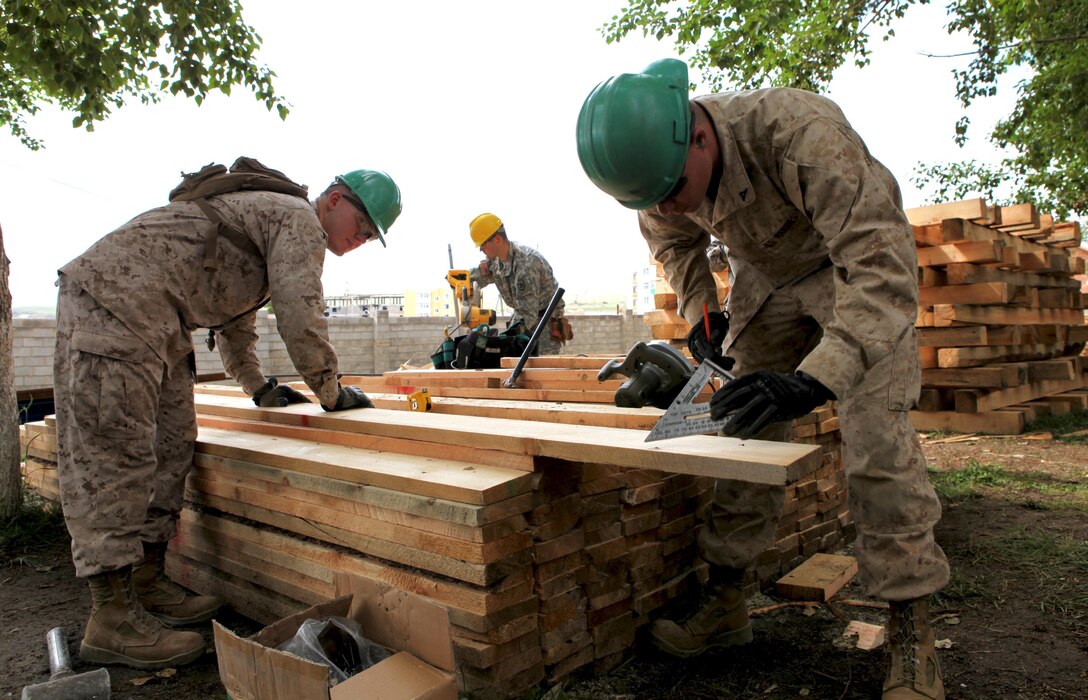 Lance Corporals Taylor Tingey and Bennett Russ (front) measure lumber, while U.S. Army Spc. Aleksandr Popov (center) cuts it, as the joint team works together July 22 to construct a handicap-accessible ramp at the the Erdmiin Oyun High School in the Nalaikh district of Ulaanbaatar during Exercise Khaan Quest 2013.  Khaan Quest is a regularly scheduled, multinational exercise co-sponsored this year by U.S. Marine Corps Forces Pacific, and hosted annually by the MAF. The intent of the ongoing engineering civic action program (ENCAP) project in Nalaikh is to provide valuable training for Mongolian and U.S. armed forces by boosting their interoperability, as well as demonstrate a mutual commitment to local community. Tingey and Russ are combat engineers with 9th Engineer Support Battalion, 3rd Marine Logistics Group, and Popov is an interior electrician with 176th Engineer Company (Vertical), 96th Troop Command, Washington Army National Guard.