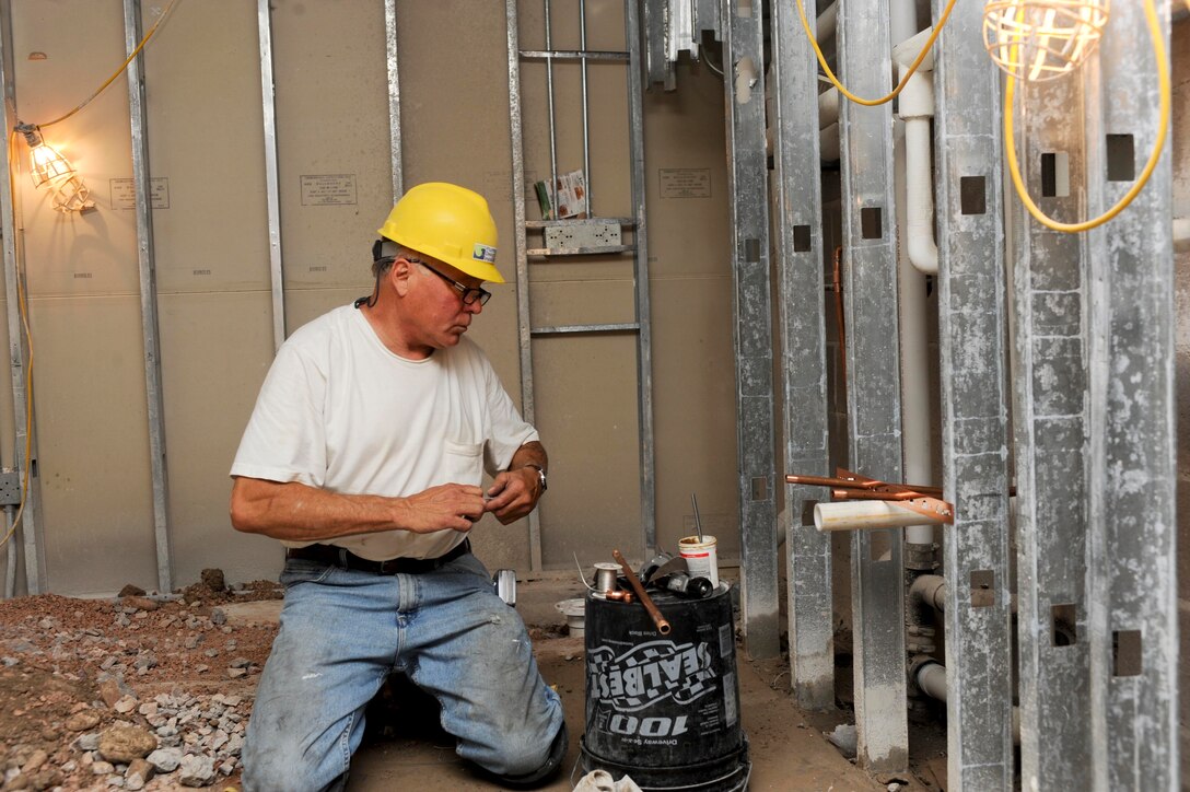 Jim Tyndall, Plumbing Design and Installation Inc. plumber, prepares to connect pieces of pipe in the wall during plumbing installation inside the Jefferson Chambers dormitory kitchenette at Ellsworth Air Force Base, S.D., July 15, 2013. Planning and installing a plumbing system that is quiet, efficient and leak-free is essential to optimal operation and aids in cost efficient maintenance. (U.S. Air Force photo by Airman 1st Class Anania Tekurio/Released) 