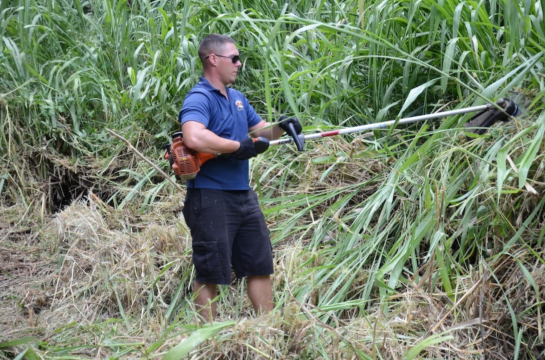 Sgt. Isreal Eschete, platoon sergeant, Remain Behind Element, 2nd Battalion, 3rd Marine Regiment, cuts plants with a weed-whacker at Heeia State Park, July 13, 2013. The Marines of the RBE, 2nd Bn., 3rd Marines and their family members joined the local community in clearing overgrown vegetation at the park. (U.S. Marine Corps photo by Kristen Wong)
