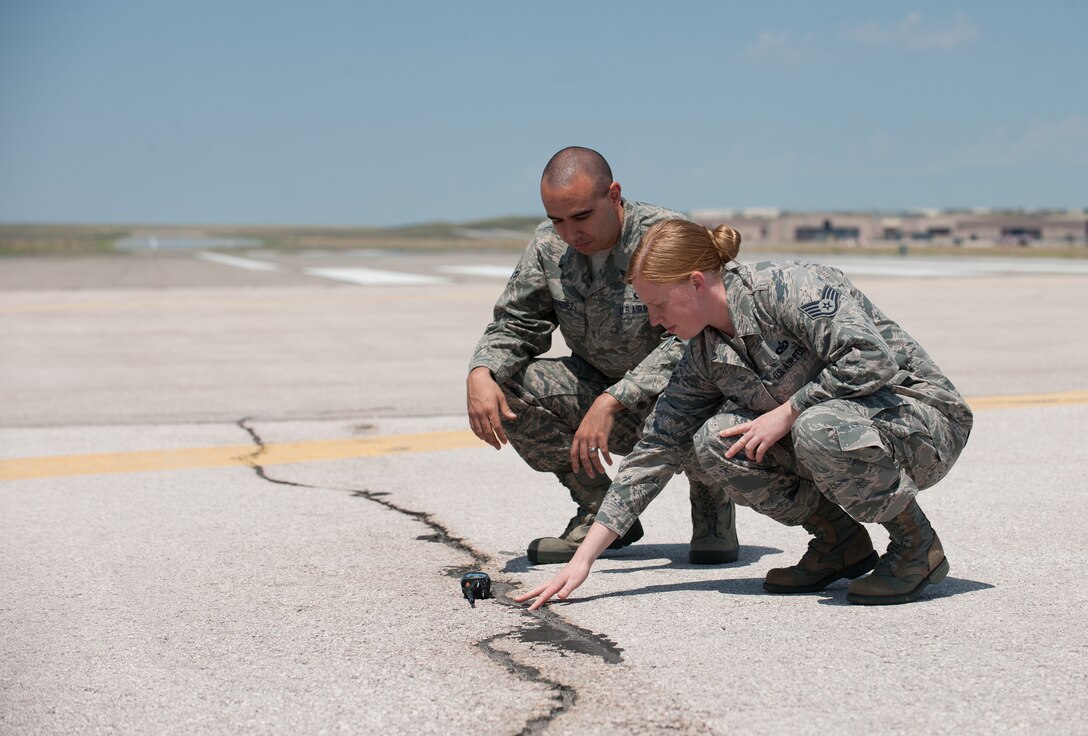 Staff Sgt. Crystal Bennoch, 28th Operations Support Squadron Airfield Management specialist, and Airman 1st Class Steven Hernandez, 28th OSS Airfield Management operations coordinator, inspect a crack on the runway to determine its severity at Ellsworth Air Force Base, S.D., July 19, 2013. Airfield management is responsible for finding and correcting flaws on the airfield to prevent safety hazards and damage to aircraft. (U.S. Air Force photo by Airman 1st Class Alystria Maurer/Released)