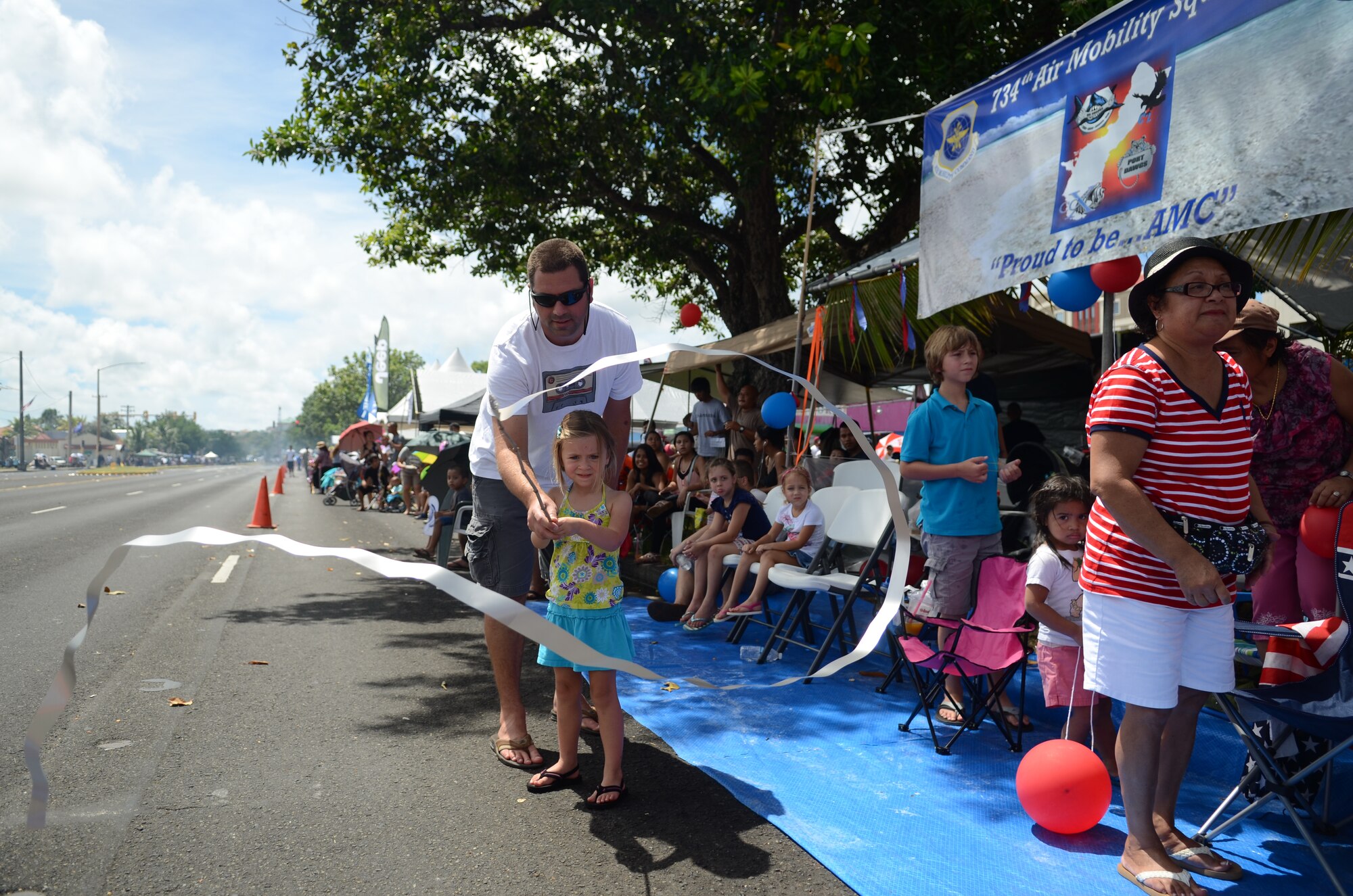 Members of the 734th Air Mobility Squadron and their families look on as the 69th Liberation Day Parade approaches their tent in Hagåtña, Guam, July 21, 2013. Formations of active-duty service members, guardsmen and reservists, including more than 140 Airmen from the 36th Wing, led the parade down the 1.2-mile route past thousands of spectators. The parade commemorated the United States freeing the island from imperial Japan’s control during the Second Battle of Guam, which began July 21, 1944, and lasted 21 days. (U.S. Air Force photo by Staff Sgt. Brok McCarthy/Released)