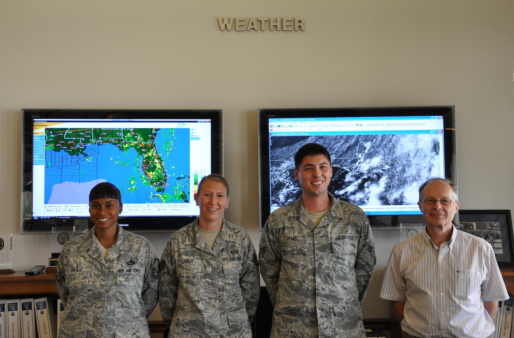 Members of the 325th Operation Support Squadron Weather Flight pose behind the front desk of their shop July 2 at the Tyndall Base Operations building. The Weather Flight is in charge of keeping an eye on the sky for dangerous weather that could impact the mission or harm the people on Tyndall. (U.S. Air Force photo by Airman 1st Class Alex Echols)