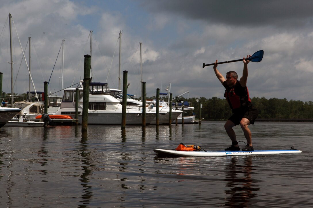 Dennis J. Yeddo, fitness facilities manager, fitness branch, Semper Fit division, Marine Corps Community Services holds his paddle above his head as he squats on his paddleboard during a Paddle Fit Boot Camp workout aboard Marine Corps Base Camp lejeune, July 23. The Paddle Fit Boot Camp workout costs $7 and is held every Tuesday from 11:30 a.m. - 12:30 p.m. at the Gottschalk Marina aboard base.