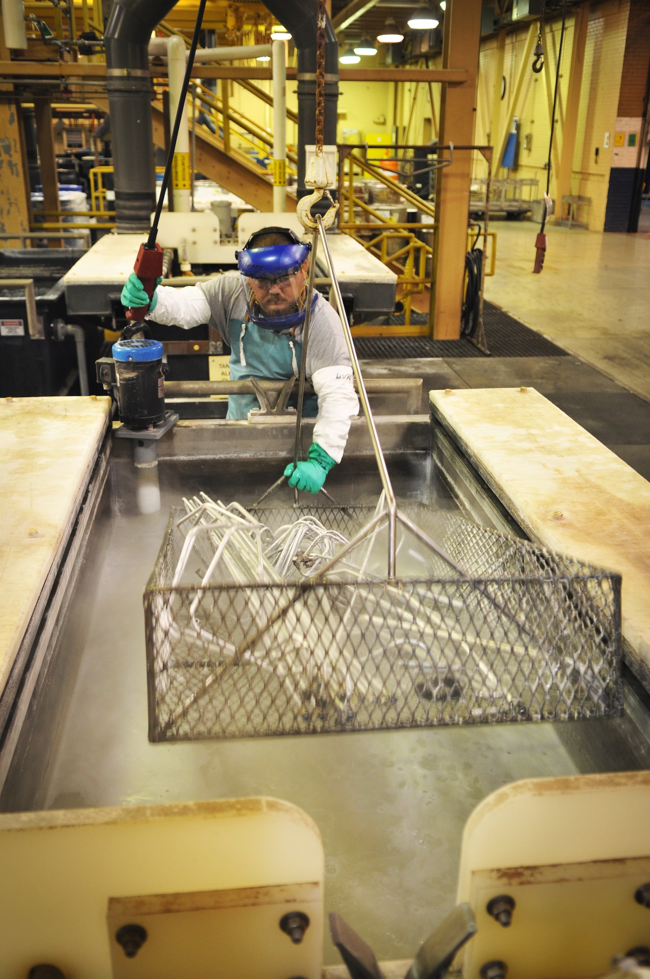 Toby Henry, an electroplater with the 548th Propulsion Maintenance Squadron, dunks a basket filled with various tubes, including aircraft oxygen tubes, into one of a series of tanks during an anti-corrosion process. The vats include an alkaline cleaner tank, a deoxidizer tank, an Alodine tank, multiple cold-water rinse tanks and a hot-water rinse tank. The process is used on other aircraft parts, as well, such as gearboxes, fan frames, and stators. (Air Force photo by Micah Garbarino)
