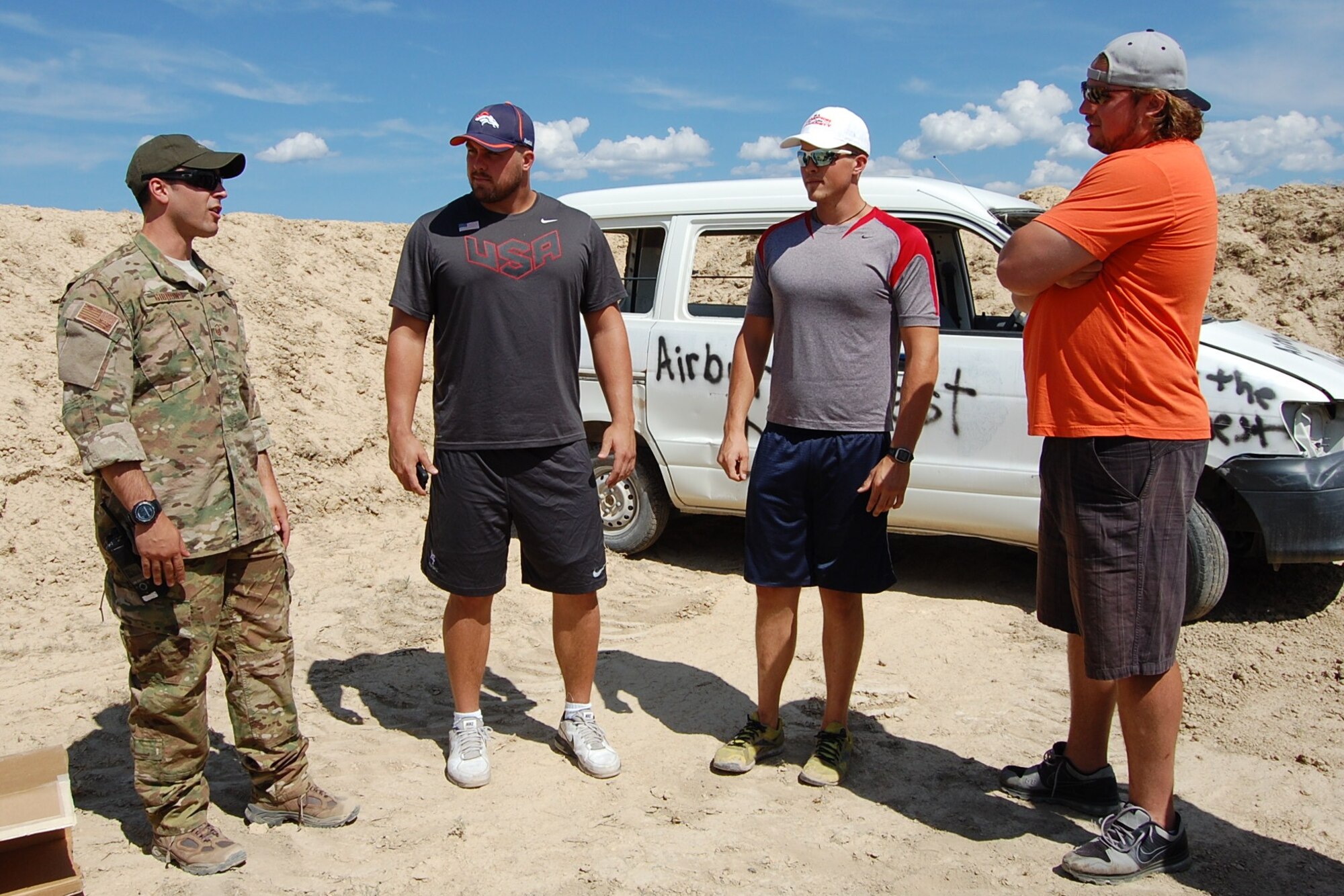 Colorado Air National Guard Master Sgt. Richard “Dick” Gibbons, 140th Explosive Ordnance Disposal Flight, briefs the day’s operations to 1st Lieutenant Ben Garland, 140th Wing public affairs officer and Denver Bronco, his brother Brandon Garland, and Denver Bronco Zane Beadles prior to detonating a hydraulic explosive in the vehicle behind them during the EOD Demo Day July 12, 2013 at Airburst Range, Fort Carson, Colo. (U.S. Air National Guard photo by Capt. Kinder Blacke)