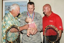 HANSCOM AIR FORCE BASE, Mass. – Former Boston Red Sox players Bob Montgomery (left) and Jim Corsi look at Capt. Jonathan Wilson’s daughter Riley who looks up at her father while posing for a photo with the 2004 and 2007 World Series championship trophies at the Hanscom Conference Center July 23. Friends and families gathered at the Hanscom Conference Center to recognize more than 50 base personnel who have returned from deployment in the past year. (U.S. Air Force photo by Linda LaBonte Britt)