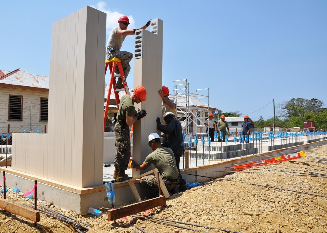 U.S. Airmen, U.S. Marines and Belize Defense Force service members work together to place exterior walls over reinforcing bars at the construction site of Crooked Tree Government Primary School. Engineers from both the U.S. and Belize are constructing various structures at schools throughout Belize as part of exercise New Horizons.  (U.S. Air Force photo by Capt. Holly Hess/Released)