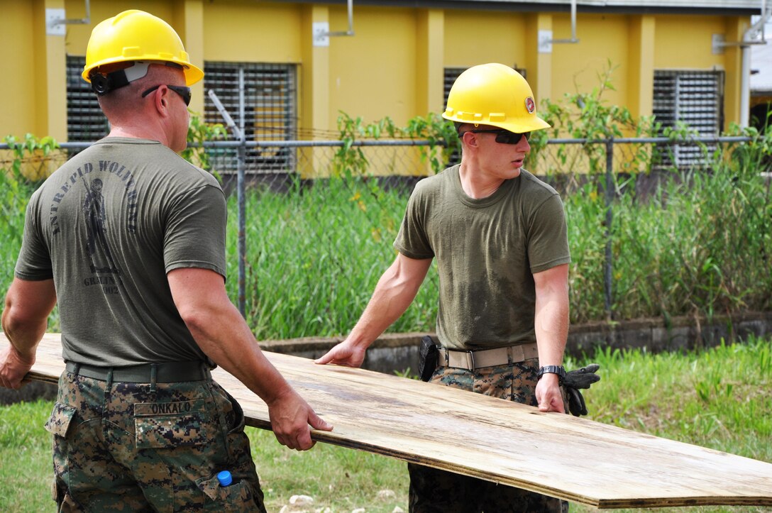 Gunnery Sgt. Eric Onkalo (Left), a combat engineer operations chief from Marine Wing Support Squadron 471, carries roof decking with Lance Cpl. Ronald Senger, a combat engineer from Marine Wing Support Squadron 471, to repair a roof at Hattieville Government Pre-School, June 4, as part of exercise New Horizons.  Engineers from both the U.S. and Belize are constructing various structures at schools throughout Belize as part of the exercise. (U.S. Air Force photo by Capt. Holly Hess/Released)
