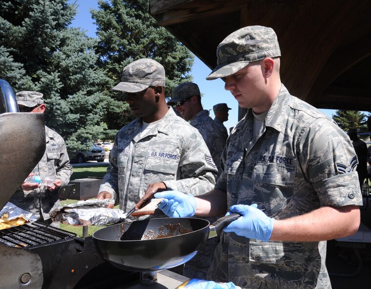 Staff Sgt. Jamel Prevost, 490th Missile Squadron chef, left, and Airman 1st Class Kyle Fritz, 490th FSS food service apprentice, cook Farsider pork chops over a grill at Sun Plaza Park during the Third Quarter Warrior Chef Competition. The two incorporated apples into their entrée by adding them to 490th chicken. (U.S. Air Force photo/Senior Airman Katrina Heikkinen)  