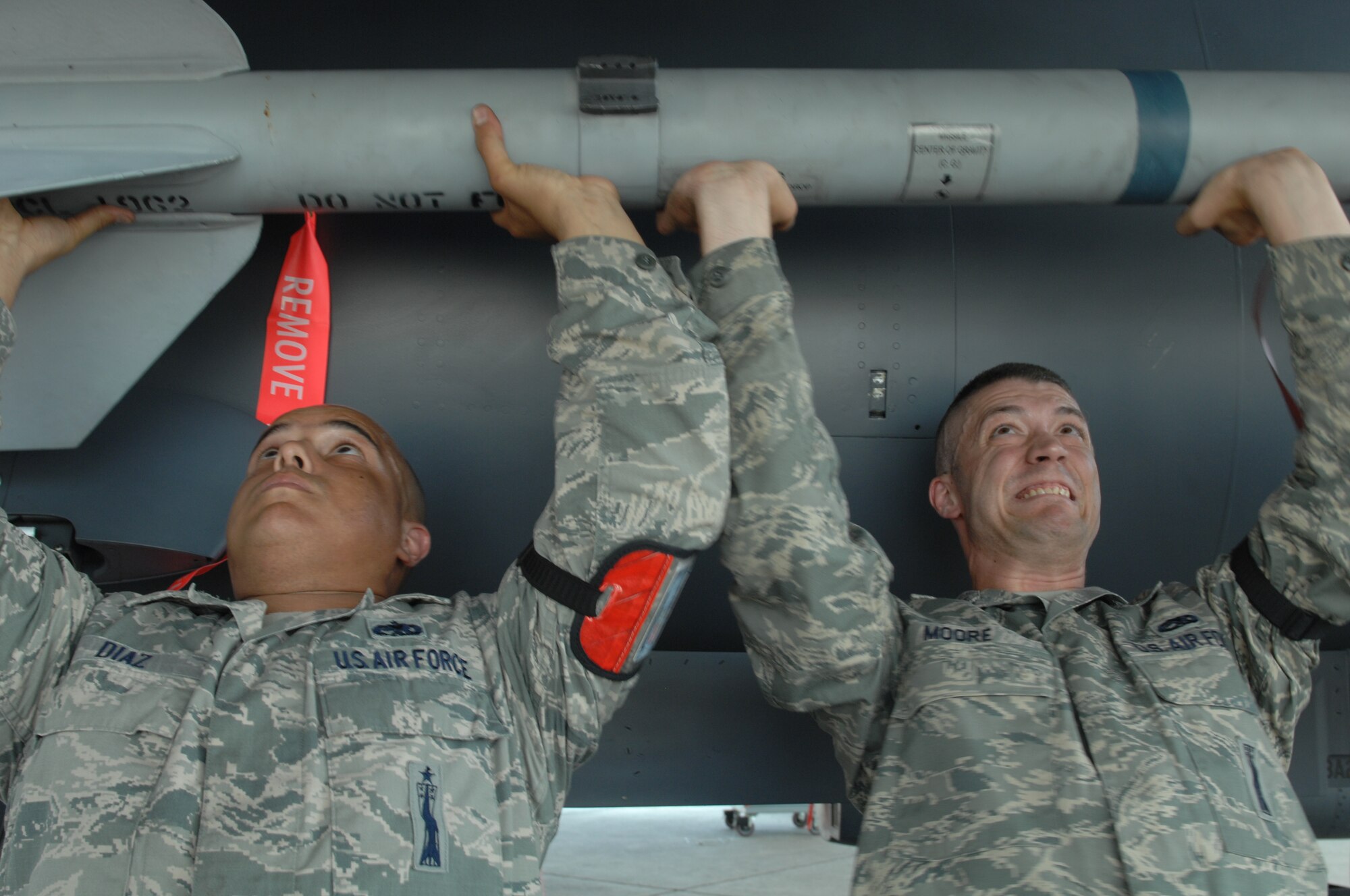 U.S Air Force Staff Sergeant Daniel Diaz Jr. and Senior Airman Jonathan Moore, 4th Aircraft Maintenance Squadron, 333rd Aircraft Maintenance Unit weapons load crew members, lift an AIM-9 missile into place on an F-15E Strike Eagle during a load crew of the quarter competition at Seymour Johnson Air Force Base, N.C., July 19, 2013.  The three-man team carried the 188-pound munition approximately 50 feet before lifting it above their heads and sliding it into position.  (U.S. Air Force photo by Airman 1st Class Brittain Crolley/Released)